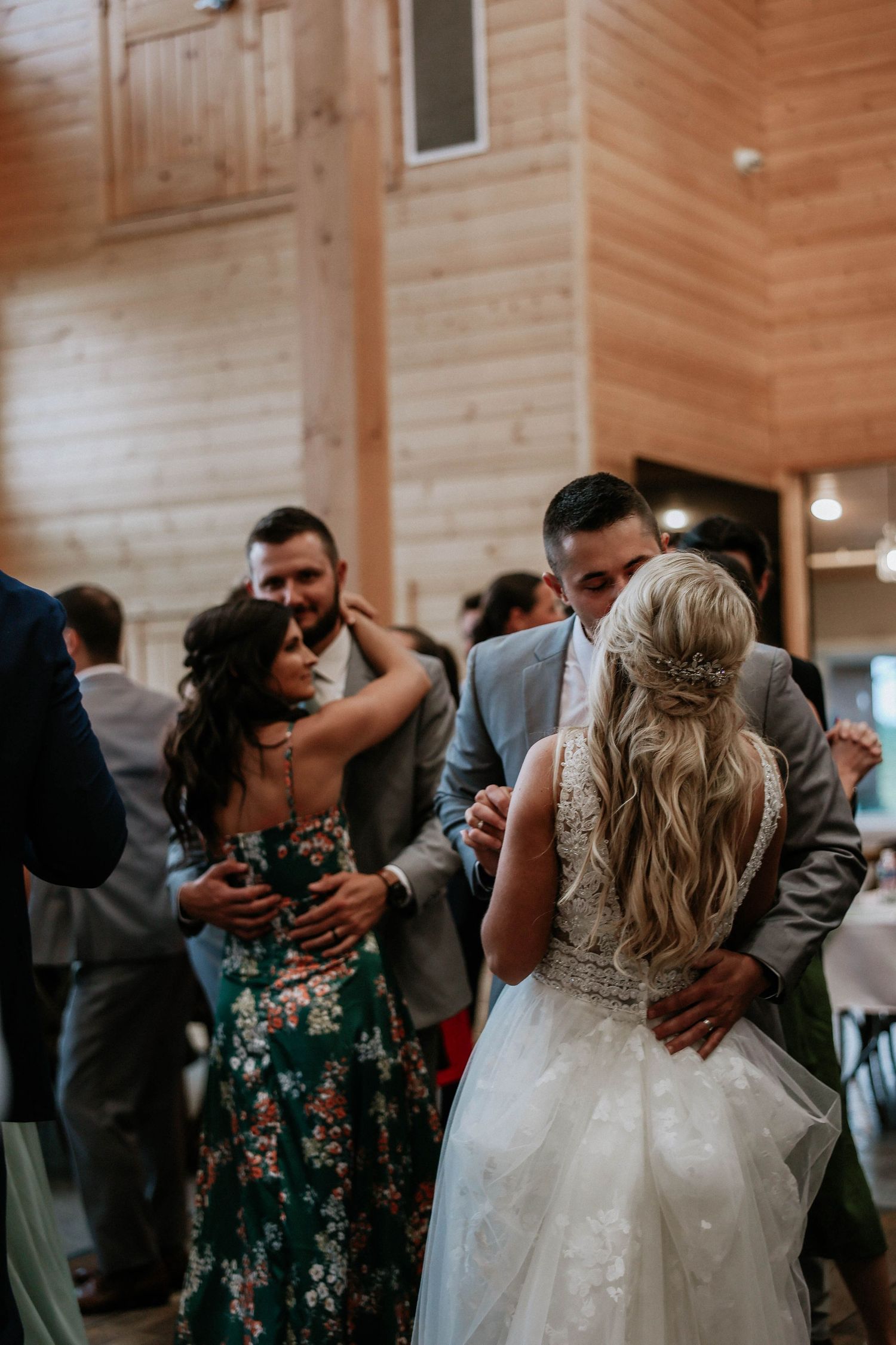 Bride and groom share first dance surrounded by wedding guests in a rustic wooden barn venue.