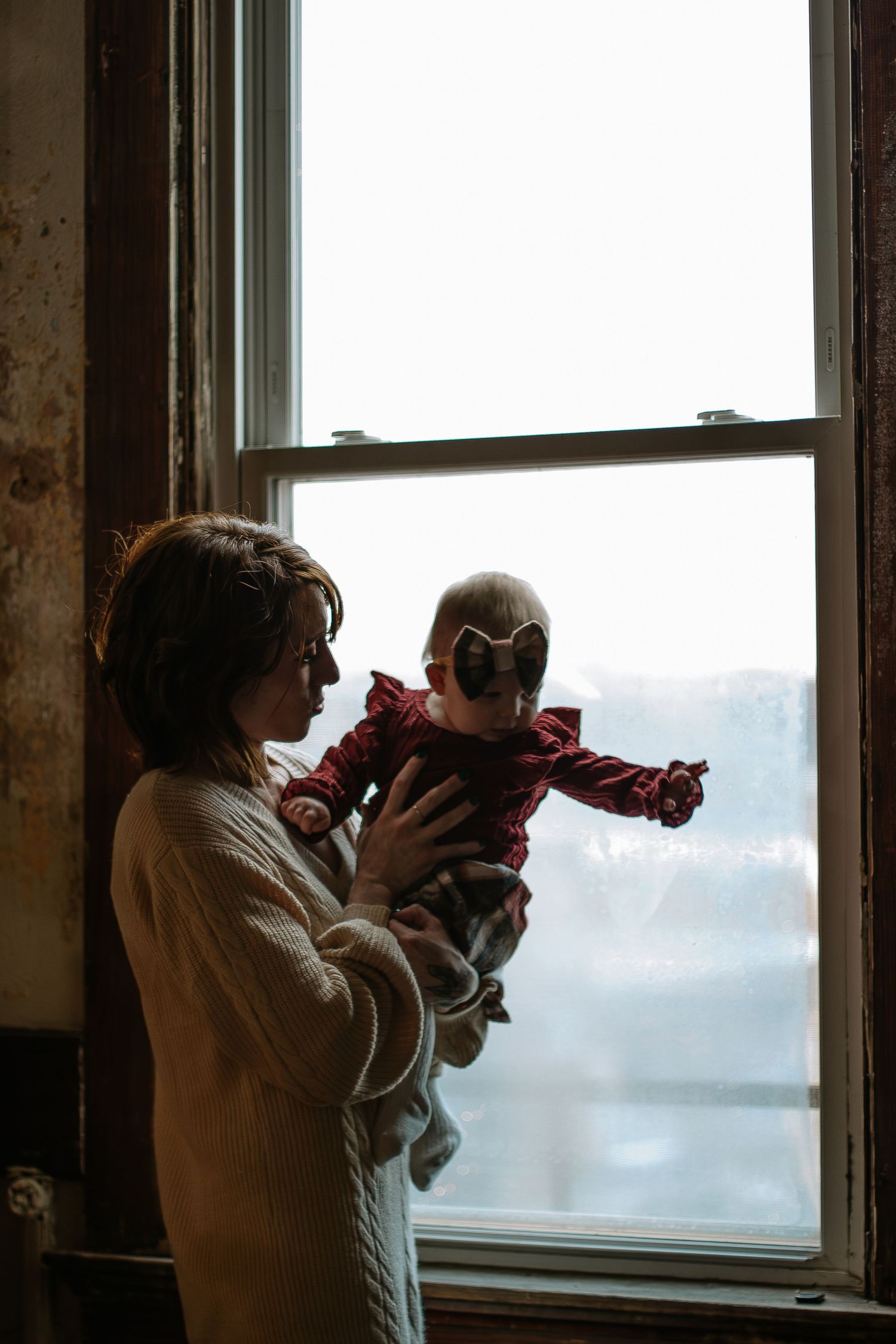 Mother holding baby girl near window in soft natural light in Cincinnati, Ohio.