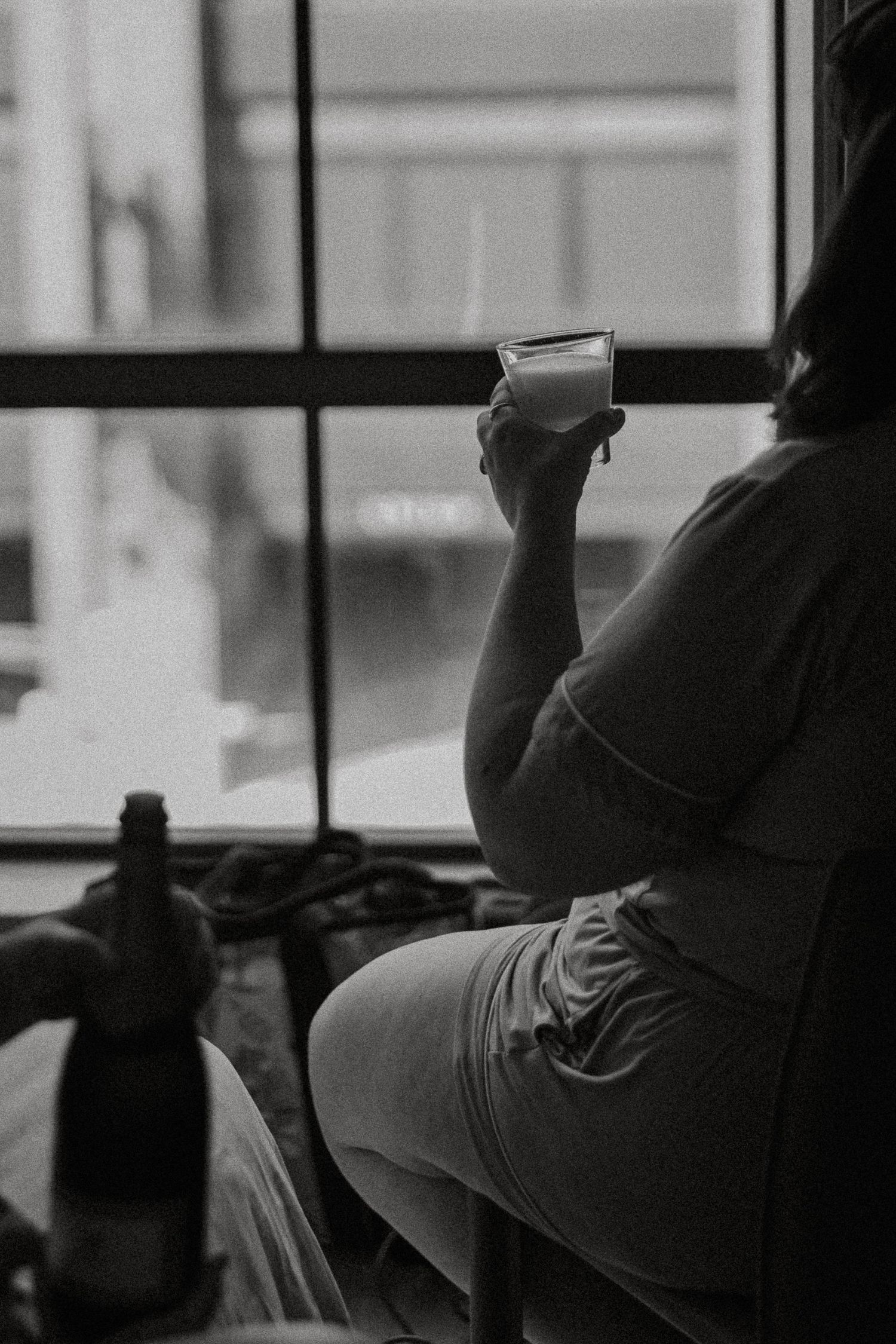 Black and white photo of woman holding coffee cup while sitting by hotel window on wedding day.