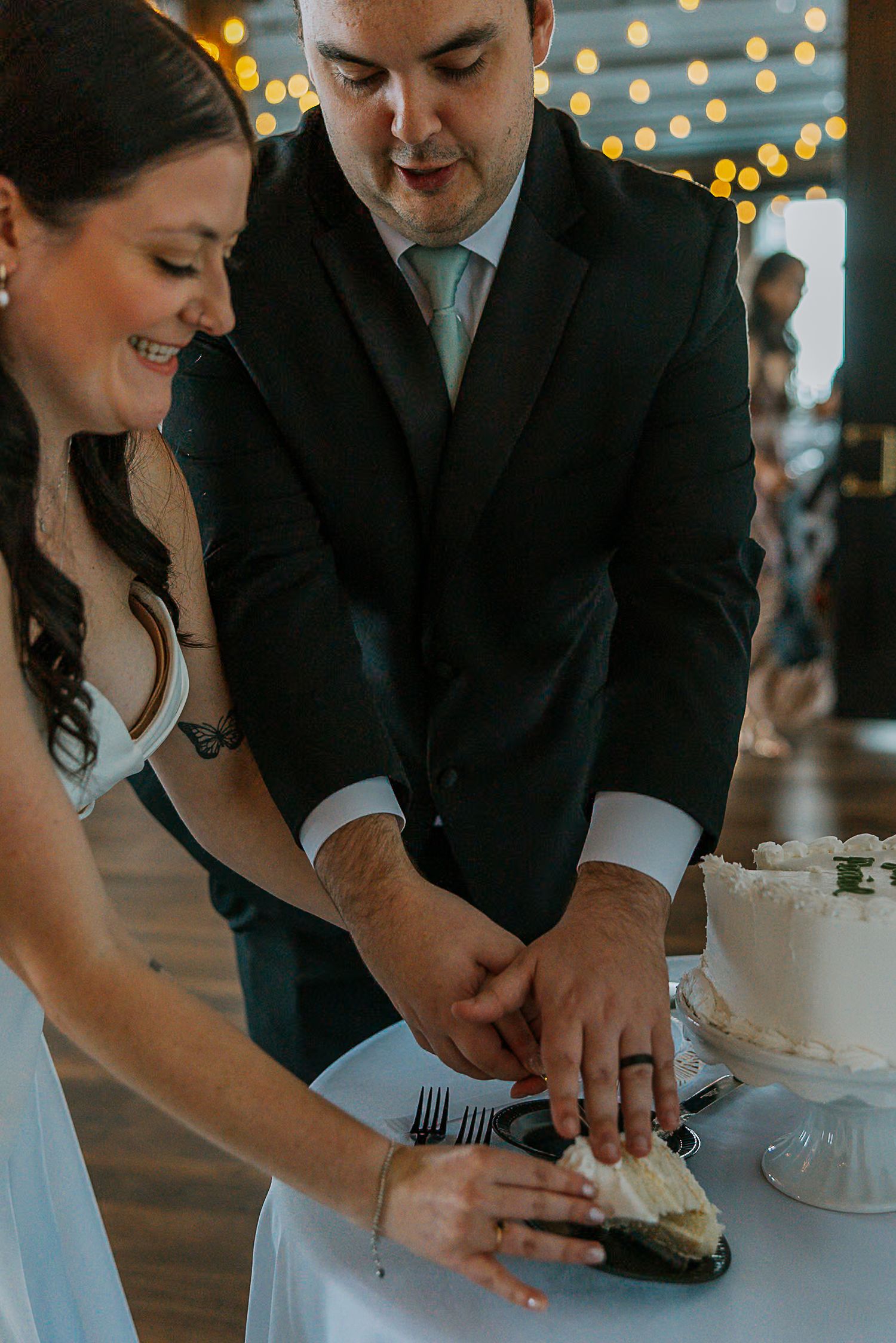 Bride and groom cutting their white wedding cake together at their reception.