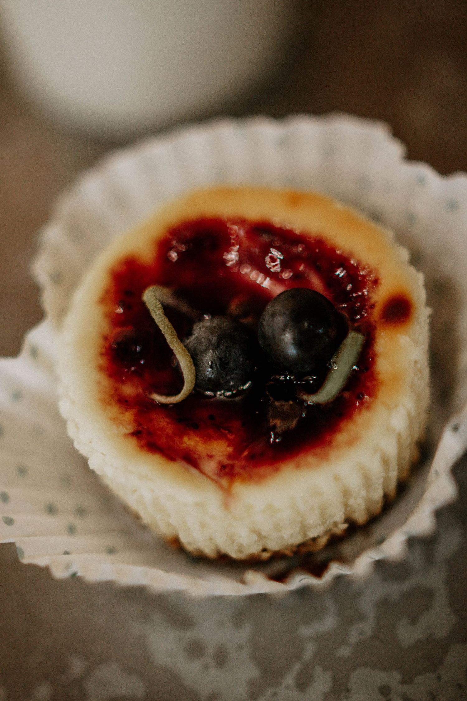 Mini cheesecake topped with blueberries and berry compote in a white paper cupcake liner.