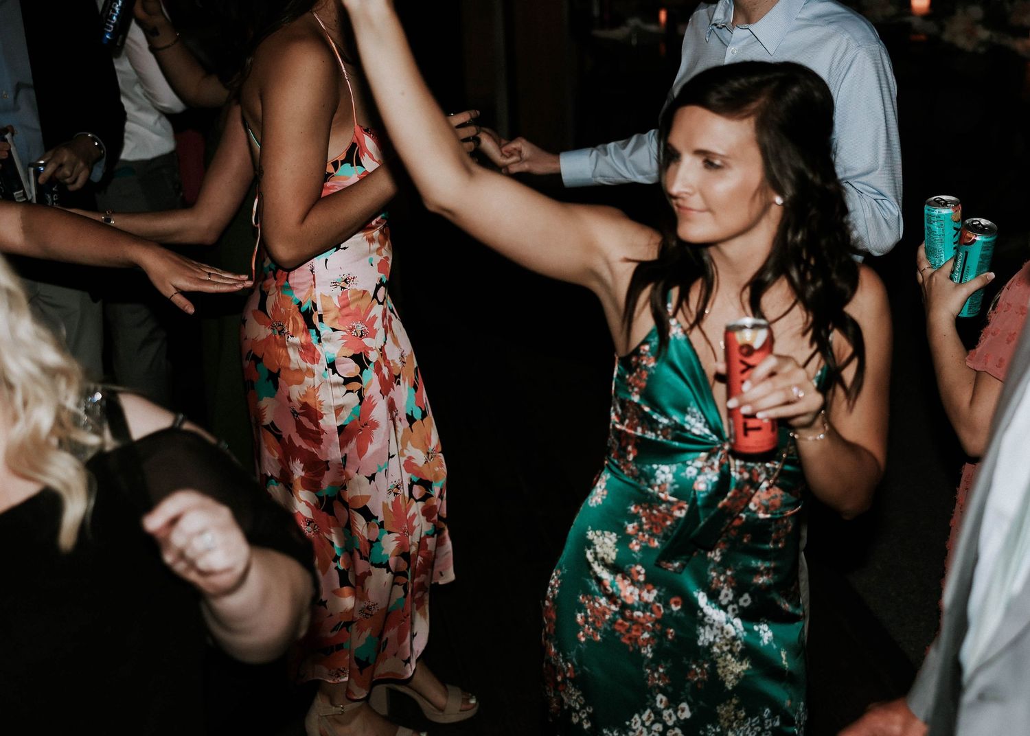 Women in floral dresses dancing and holding drinks at a lively wedding reception party.