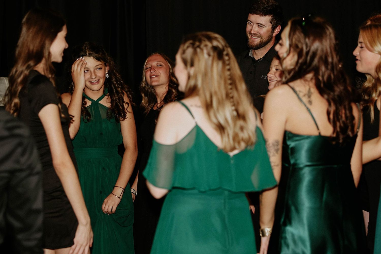 Group of women in elegant green dresses laughing and socializing at a formal event or wedding reception.