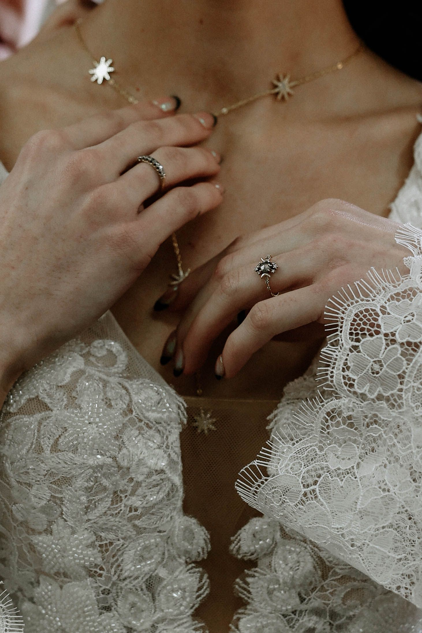 Close-up of bride's hands wearing elegant star rings and delicate gold star necklace with white lace wedding dress.