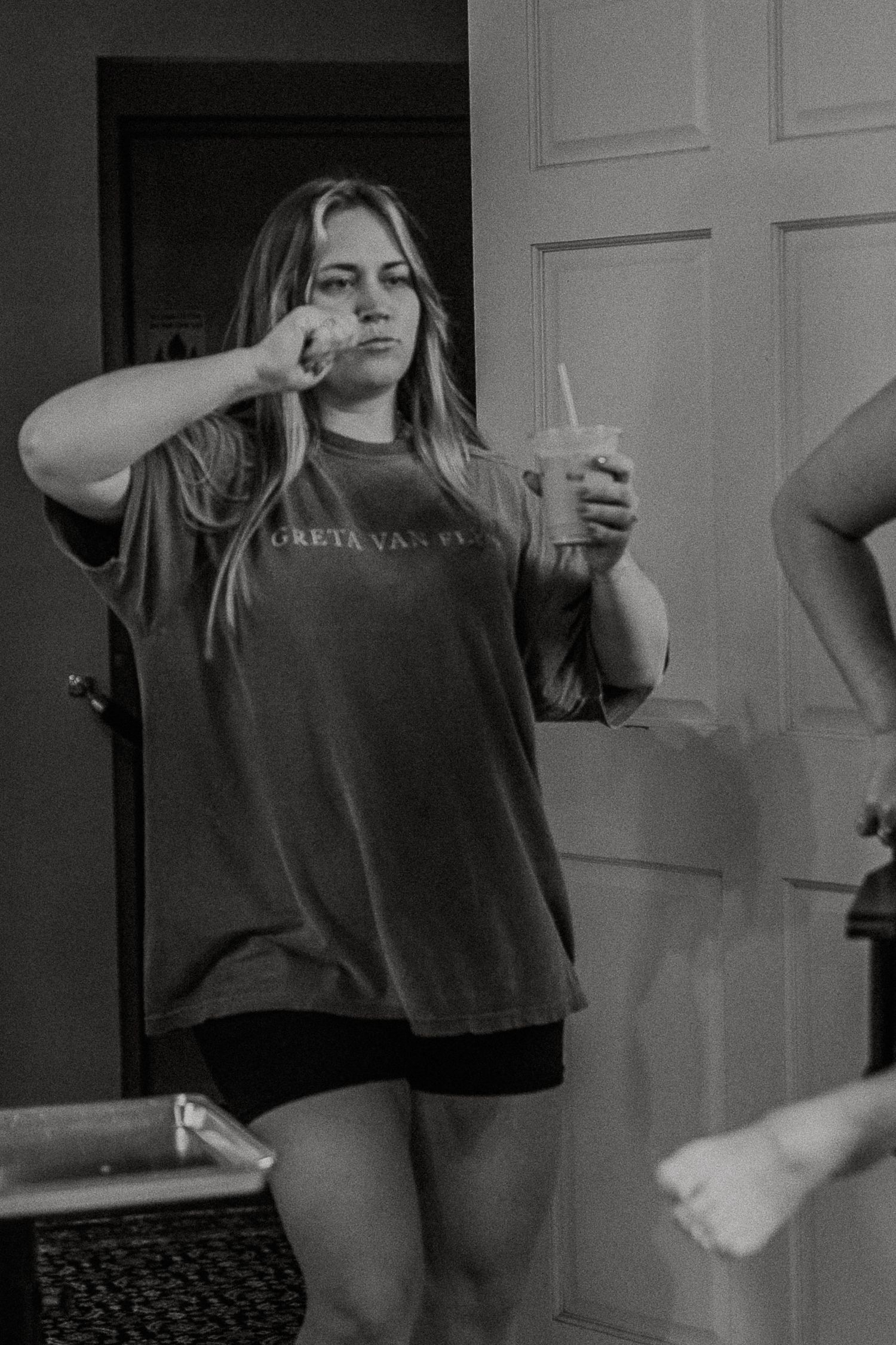 Black and white photo of a woman in Greta Van Fleet shirt holding an iced drink.