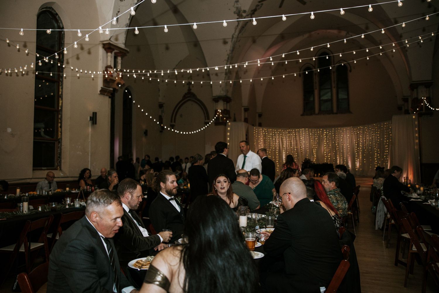 Elegant wedding reception hall with string lights, arched ceilings, and guests dining at tables at Urban Artifact in Cincinnati, Ohio