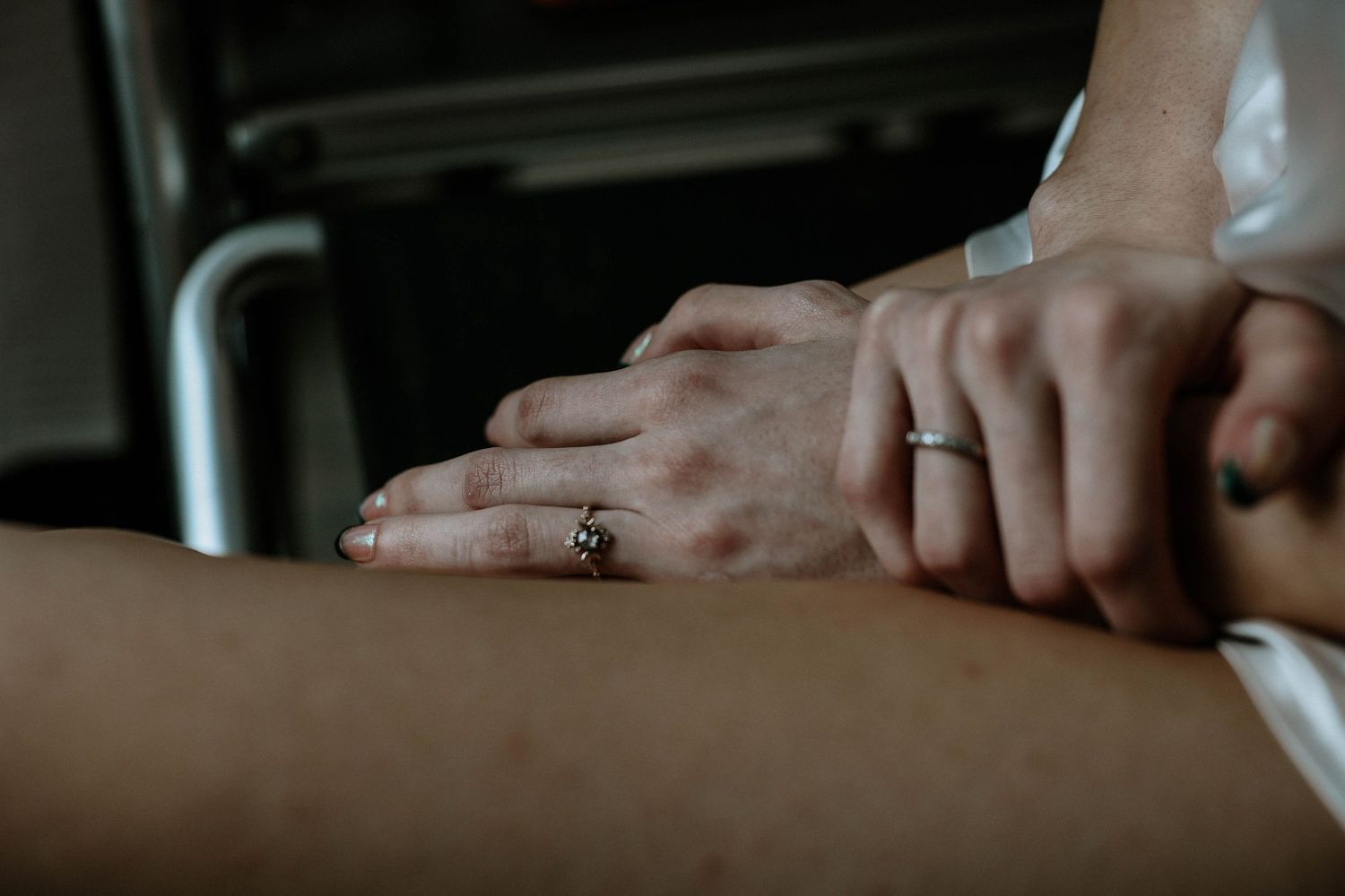 Close-up of two hands gently touching, both wearing silver rings, against a dark background.