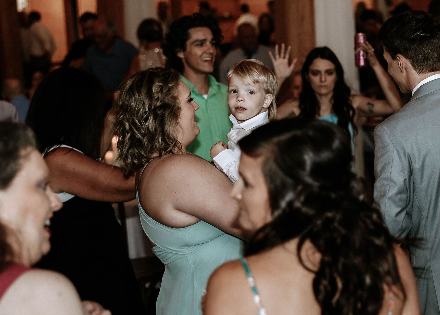 Guests dancing and socializing at a wedding reception, including a woman holding a young child in a white outfit.