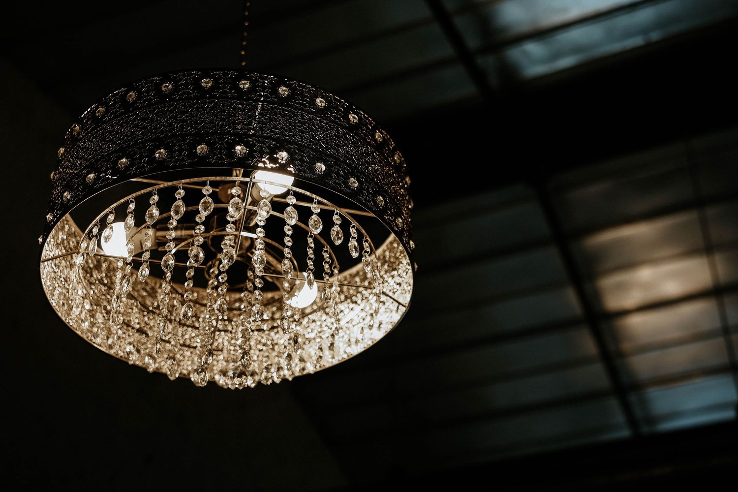 Elegant crystal chandelier with warm glowing bulbs hanging from a dark ceiling, adding glamour to interior decor.