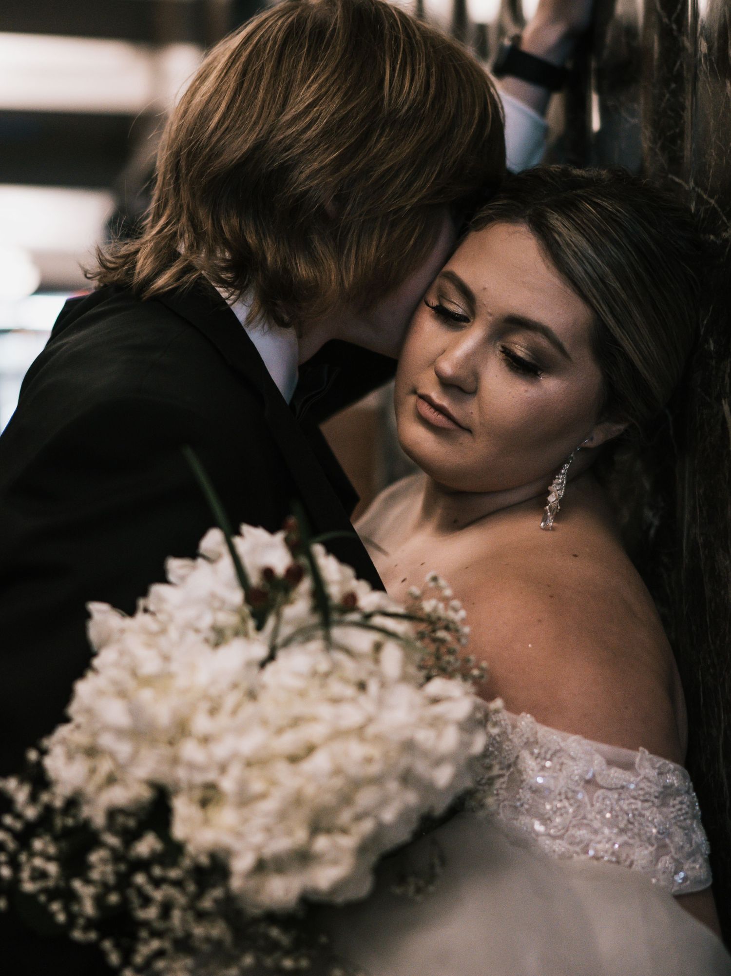 Bride and groom share an intimate moment, bride holding white floral bouquet in elegant off-shoulder gown.