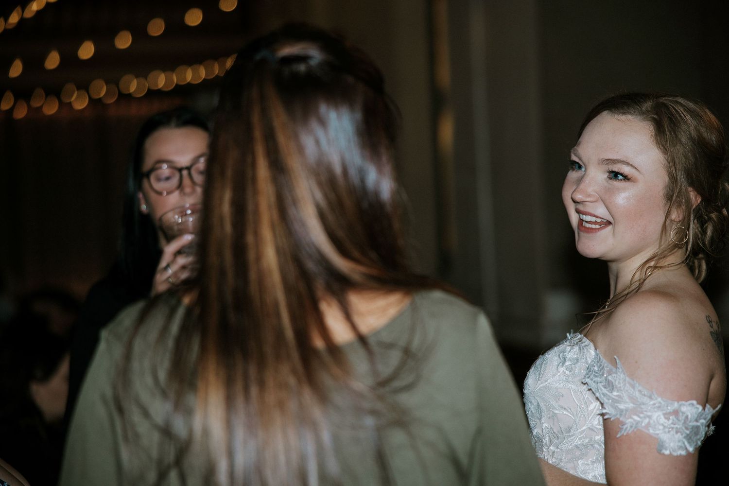 Bride in lace off-shoulder wedding gown smiling warmly while chatting with guests at wedding reception at Urban Artifact in Cincinnati, Ohio