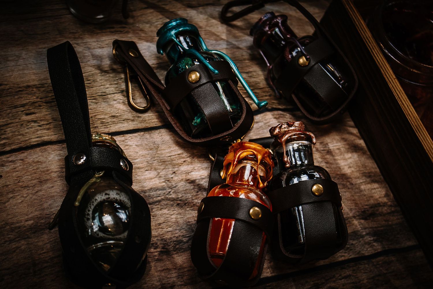 Four decorative glass bottles in leather holsters displayed on a rustic wooden surface, featuring teal, amber, and dark hues.