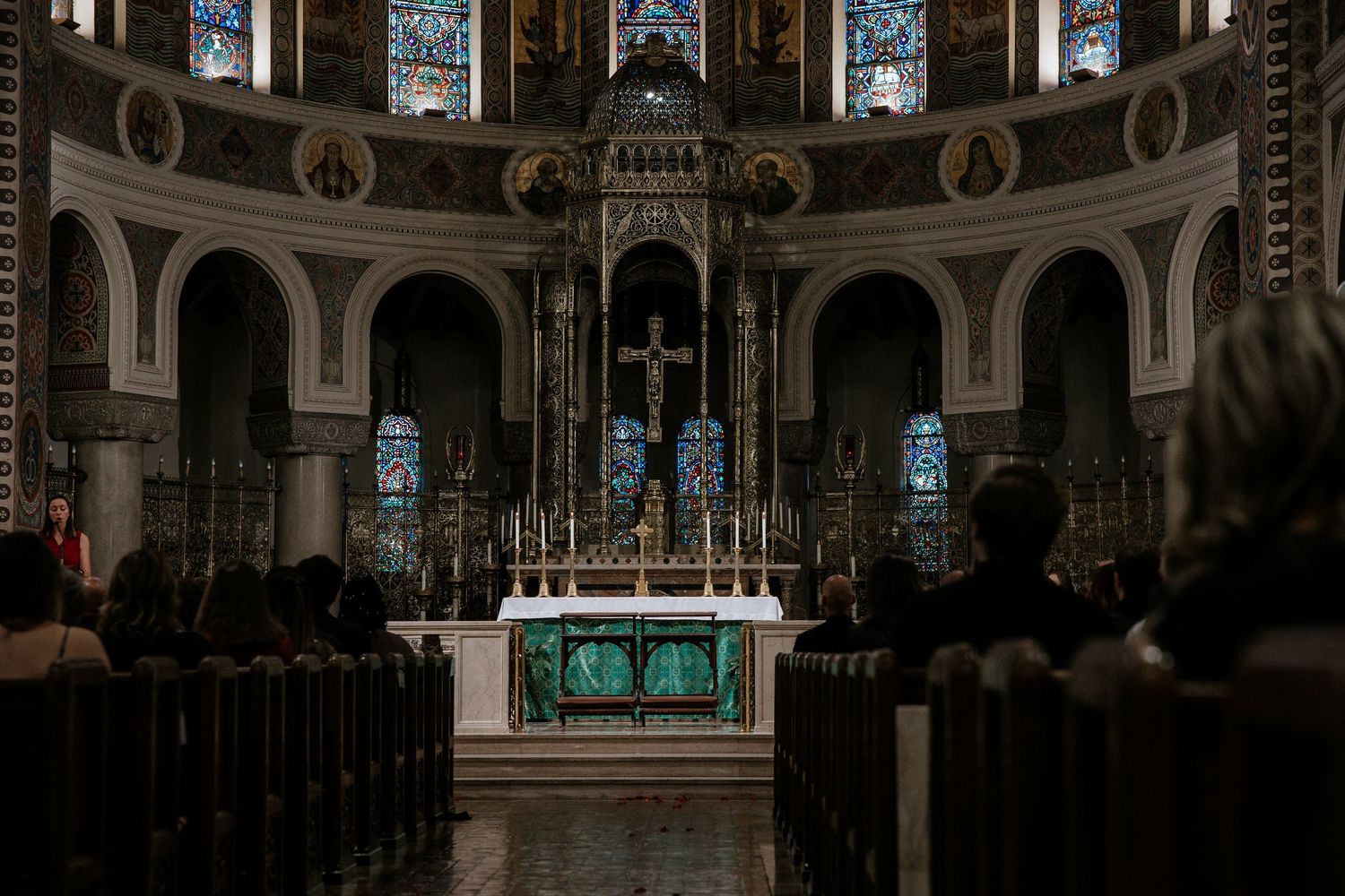 Guests seated in wooden pews face ornate church altar with stained glass windows during ceremony in Cincinnati, Ohio