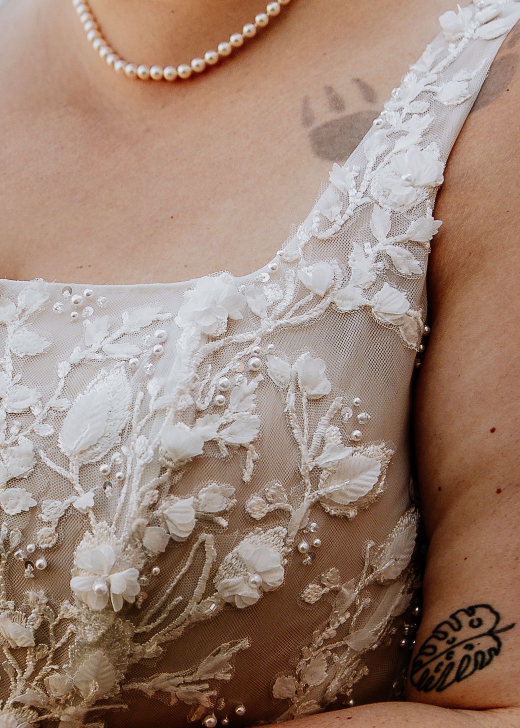 Close-up detail of white floral lace embroidery on bridal gown with pearl necklace.