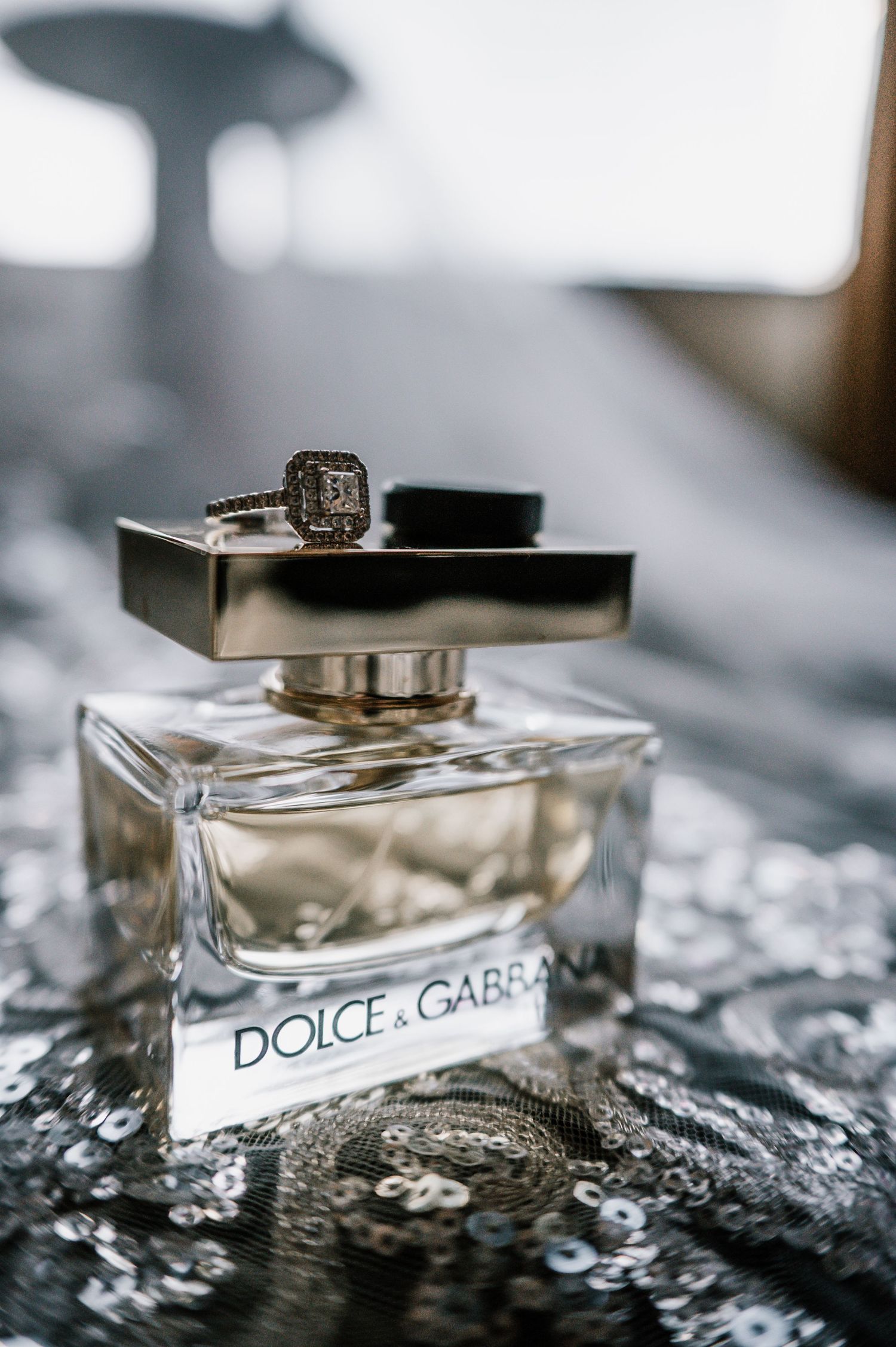 Dolce & Gabbana The One perfume bottle with a diamond engagement ring on sequined fabric at Central Park in New York City.