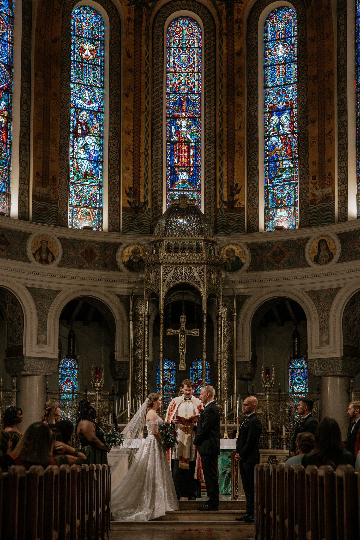 Bride and groom stand at altar beneath stunning stained glass windows during church wedding ceremony in Cincinnati, Ohio