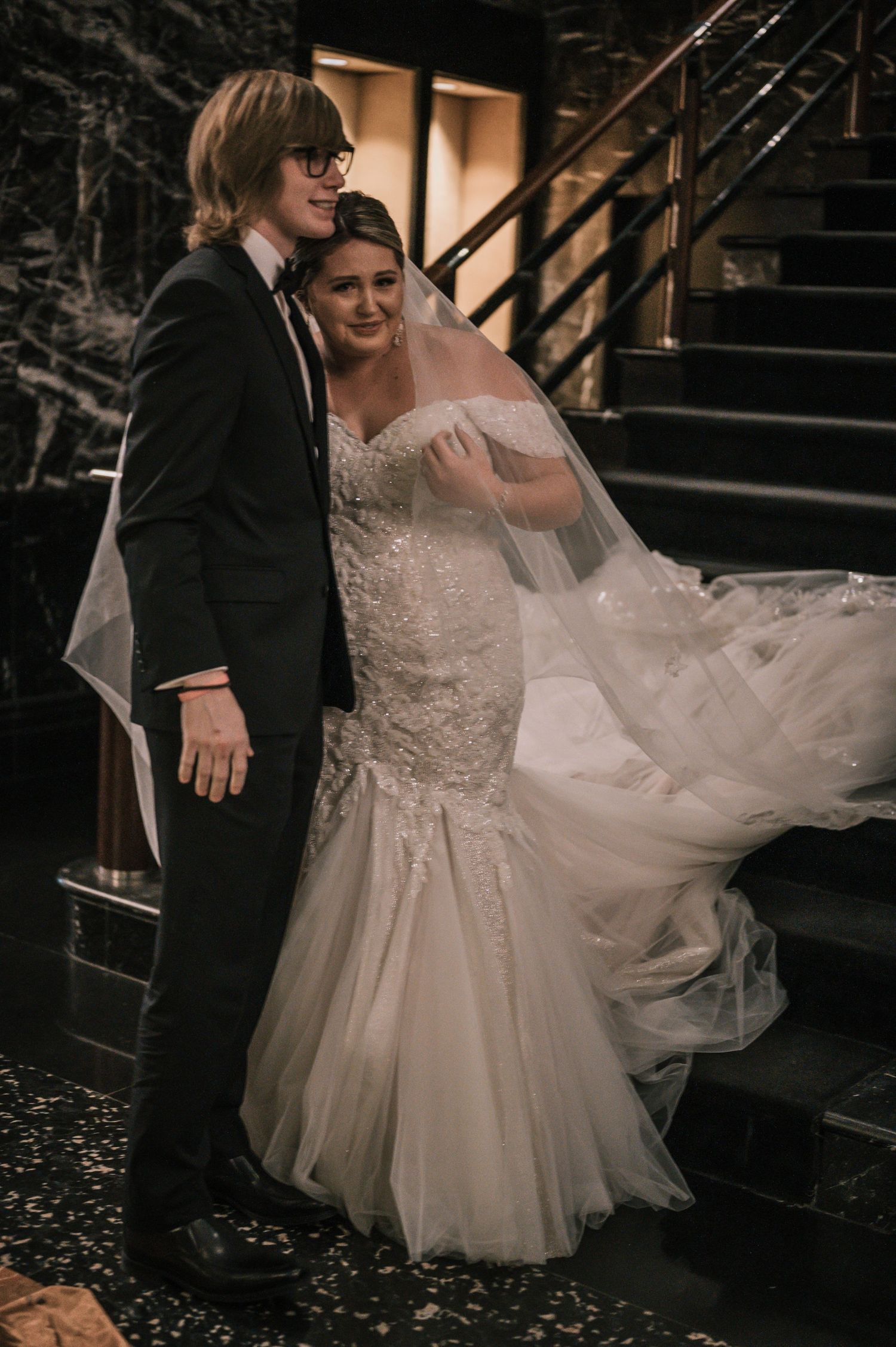 Bride and groom posing together on marble staircase, bride wearing lace mermaid wedding dress with veil.