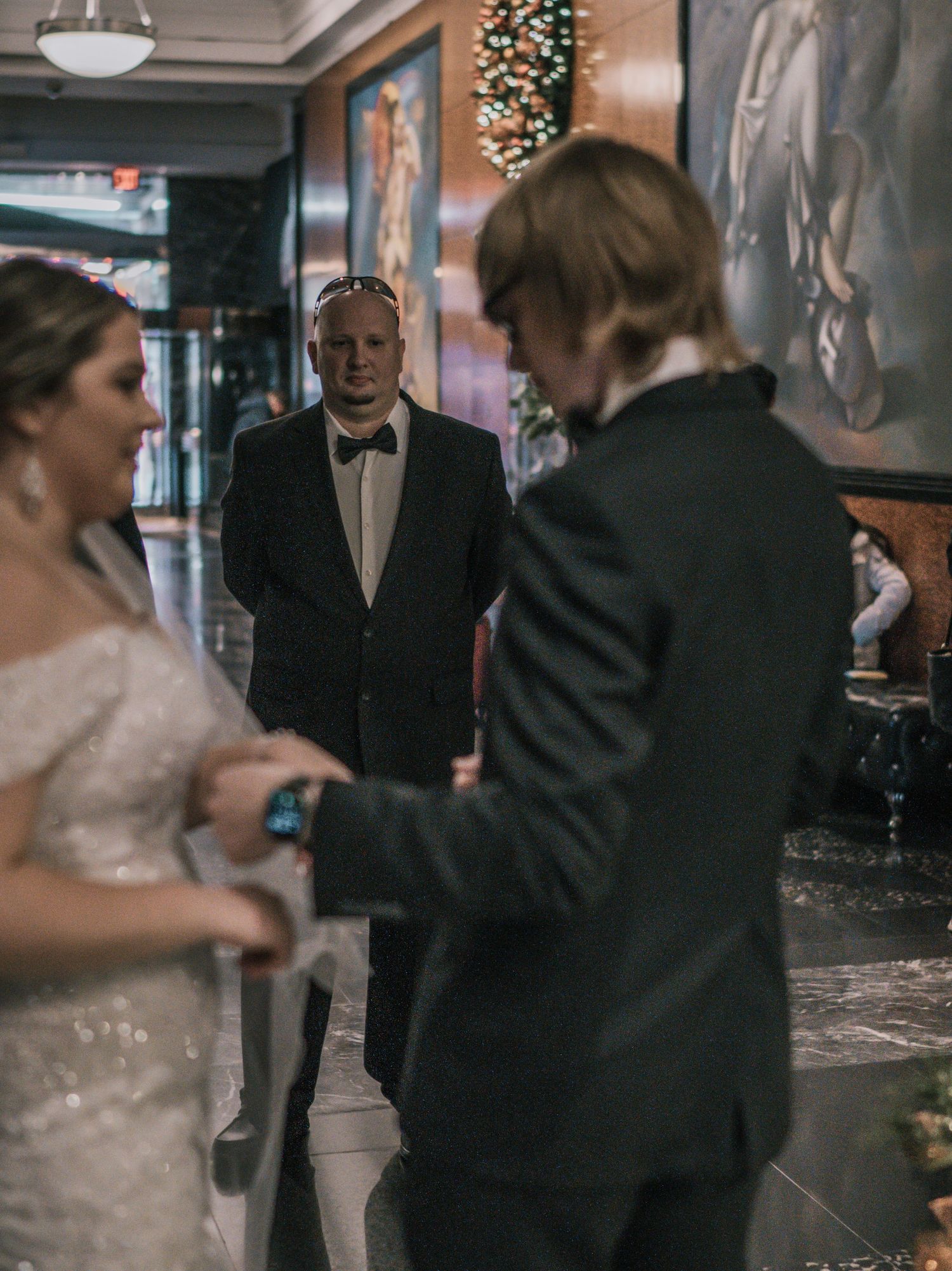 Bride and groom exchange vows as officiant watches in decorated holiday hotel lobby setting.