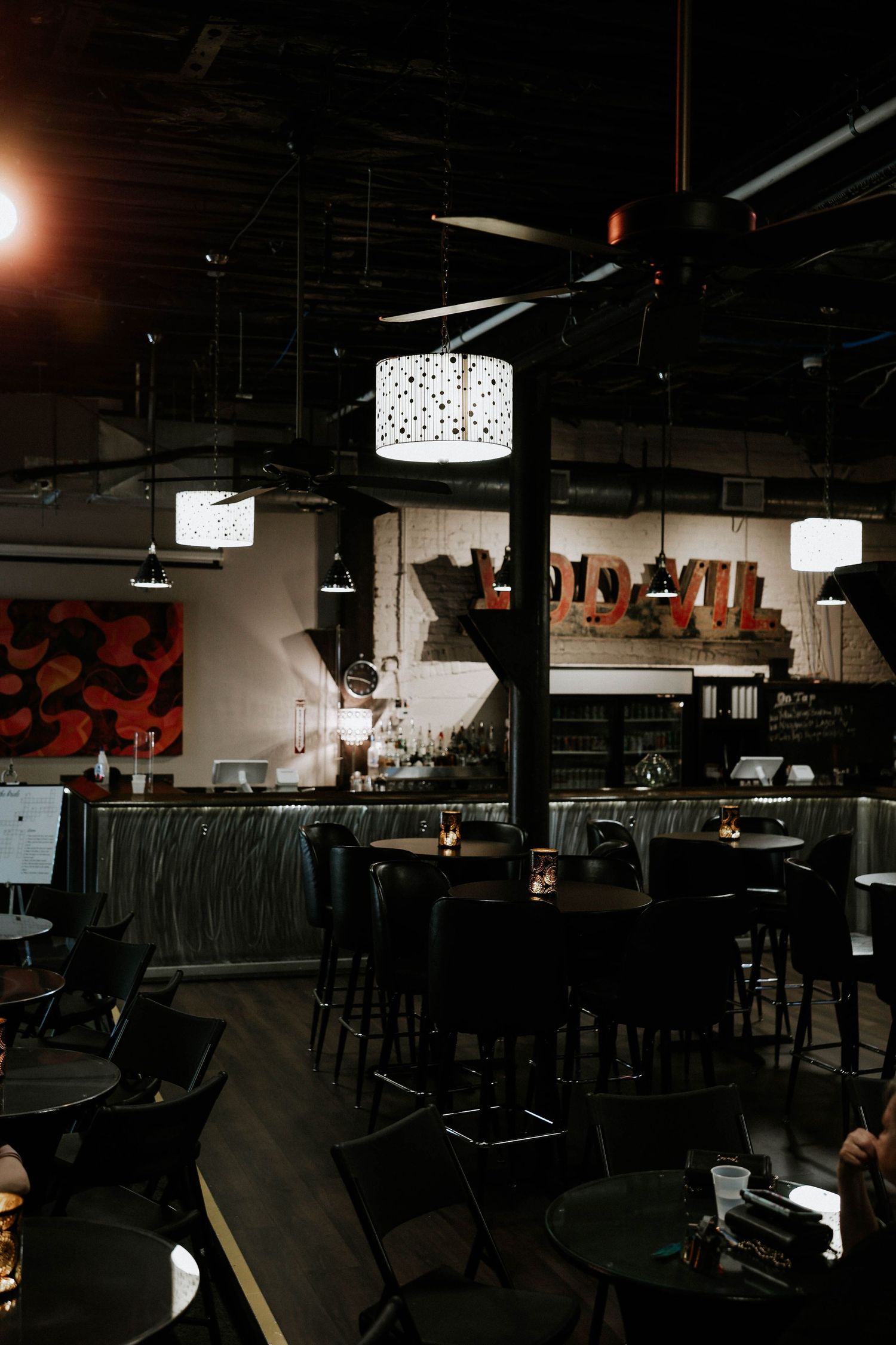 Dimly lit modern restaurant interior with dark furniture, pendant lights, and vintage signage on a brick wall.