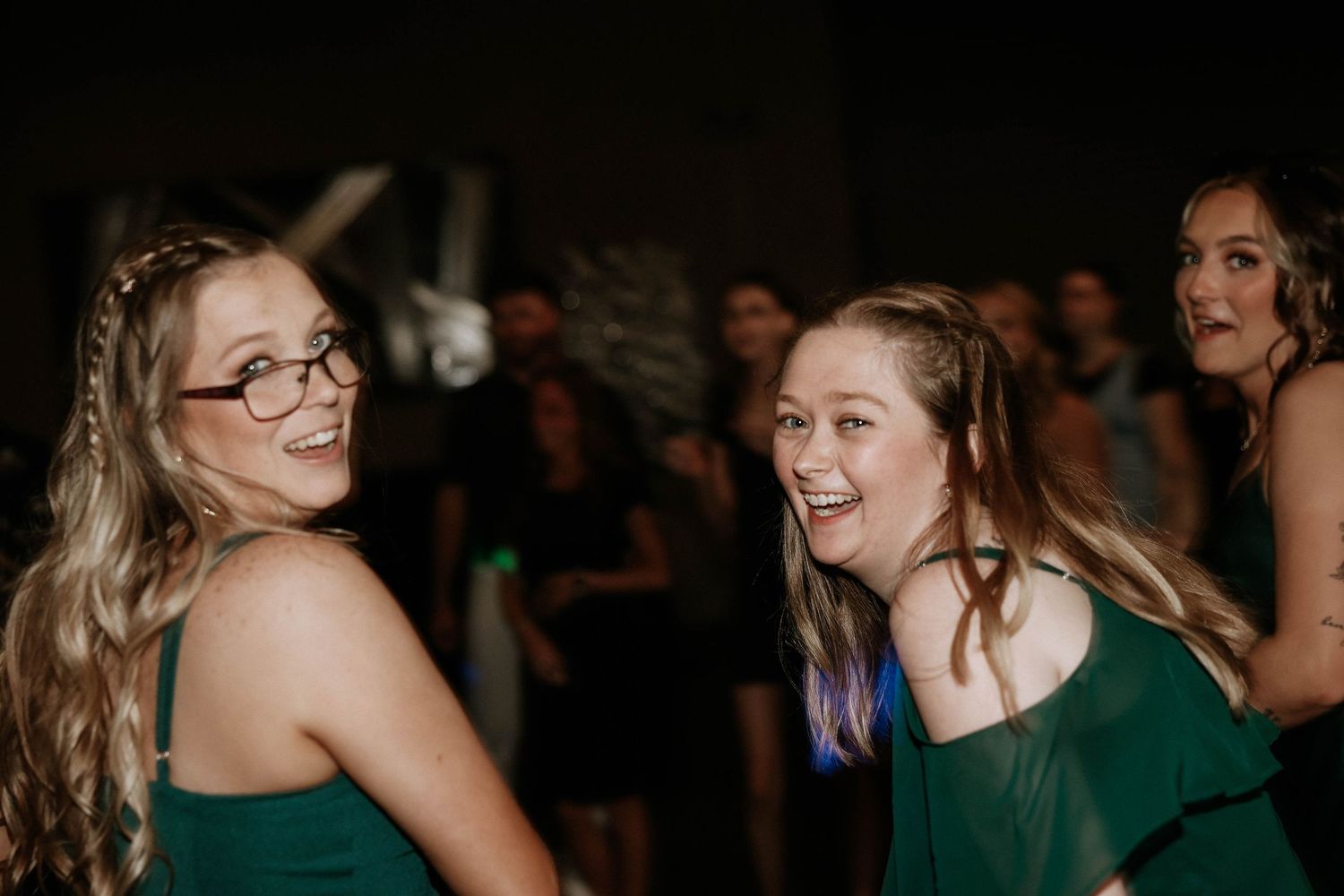 Two women in green dresses laughing and dancing together at a wedding reception.