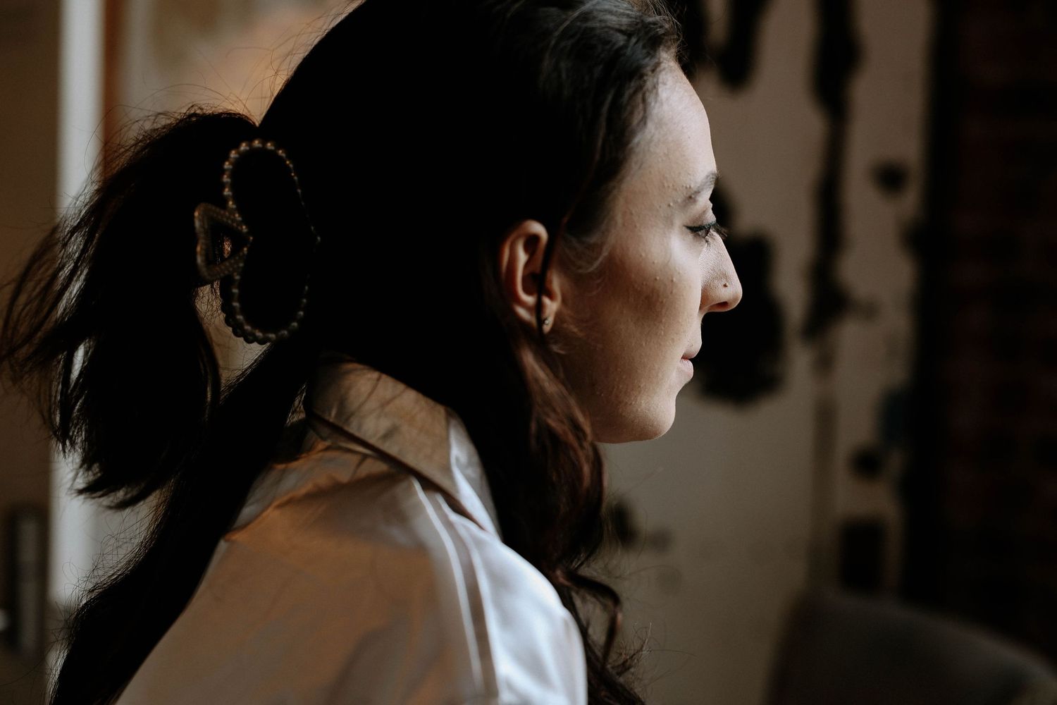 A close-up profile of a woman with dark hair and hoop earrings in soft lighting.