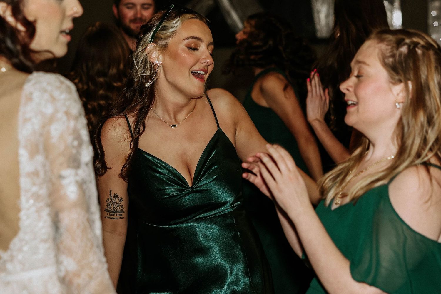 Women in elegant green satin dresses dancing and laughing joyfully at a wedding reception celebration.
