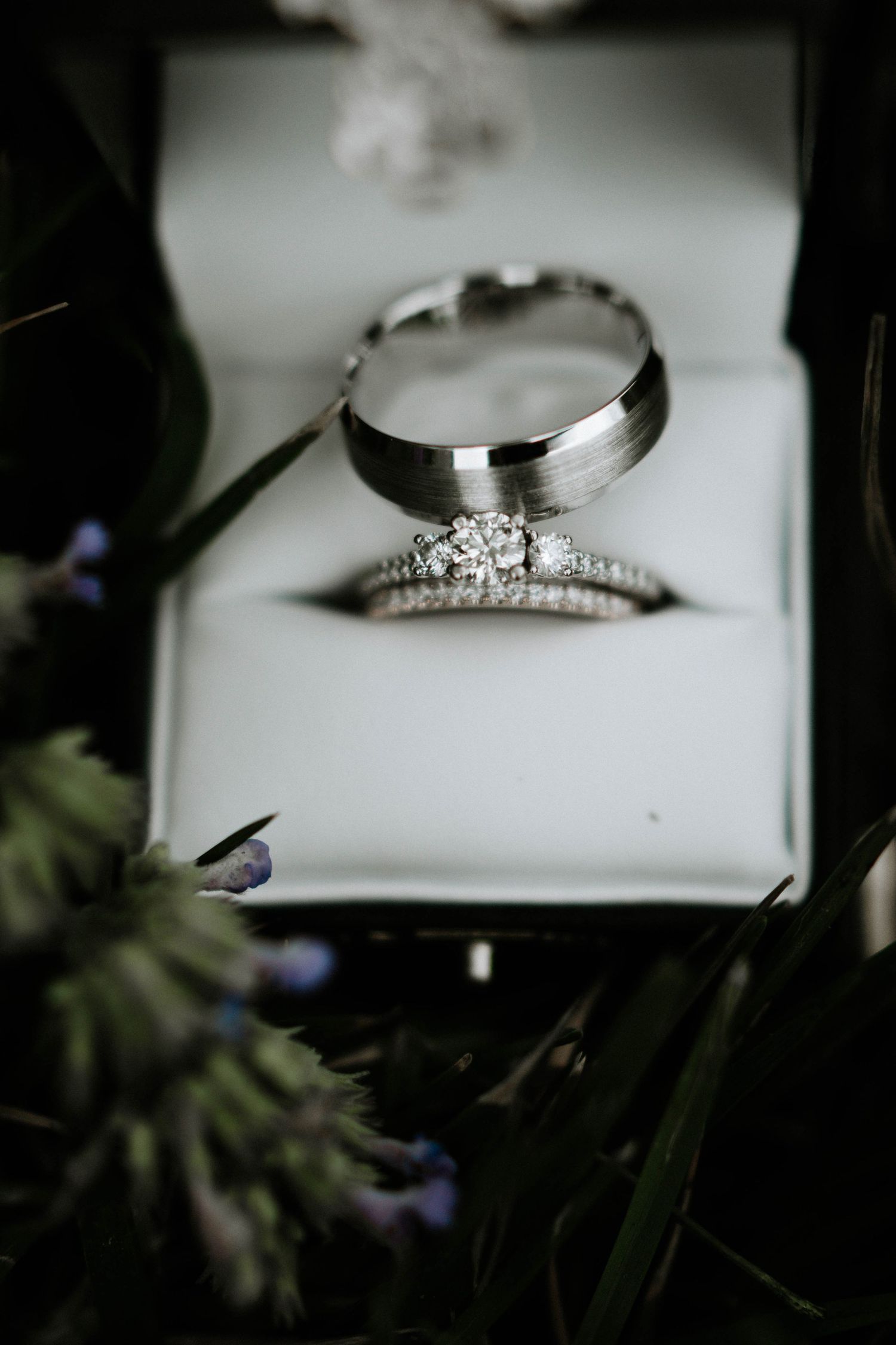 Diamond engagement ring and wedding band set displayed in a white jewelry box surrounded by soft floral greenery.