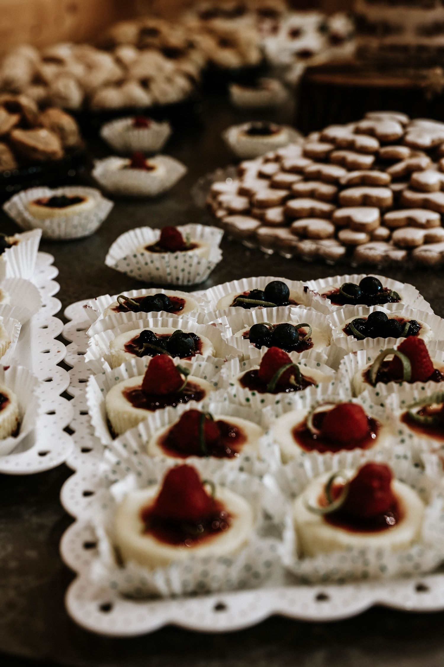 Assorted mini desserts including cheesecake bites topped with fresh berries and berry sauce displayed on decorative white doily trays.