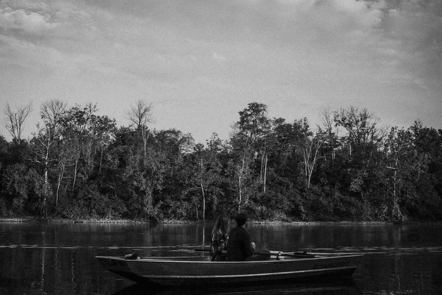 A solitary person sits in a rowboat on a calm lake surrounded by trees in a black and white photo in Cincinnati, Ohio