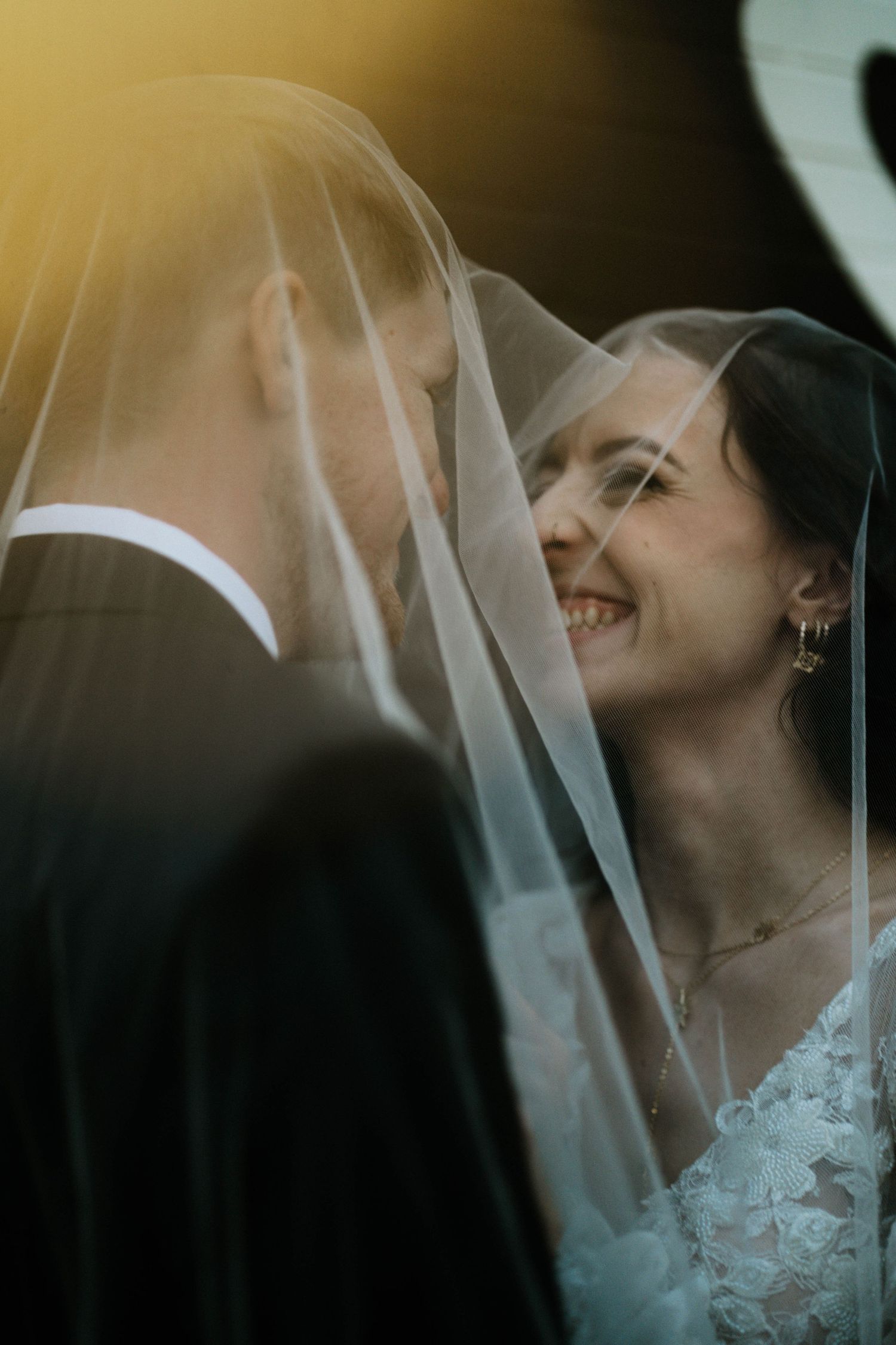 Bride smiling under veil with groom in golden sunset light during romantic wedding portrait session at The Brightside in Dayton, Ohio