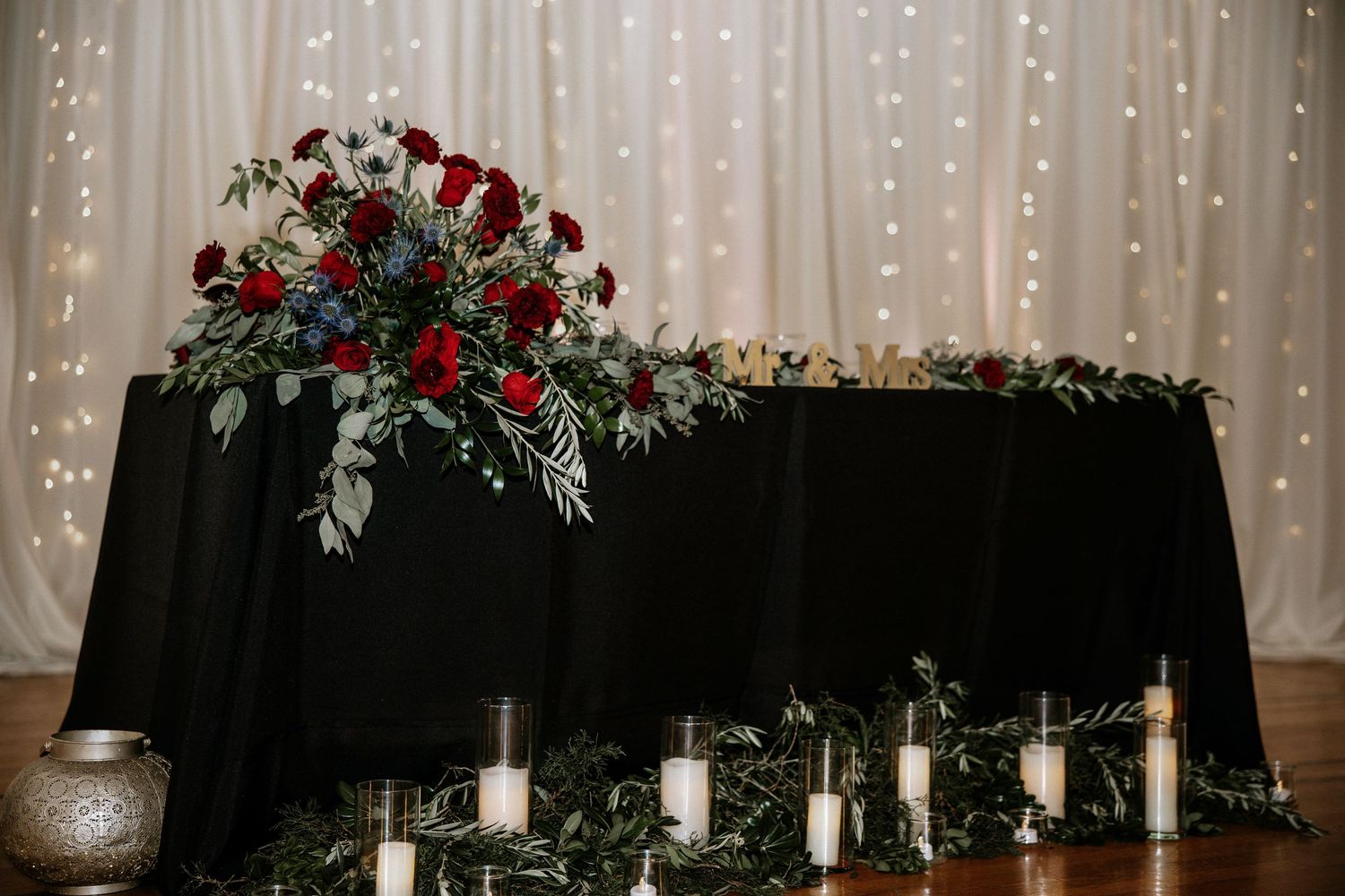 Wedding sweetheart table with black linen, red roses, greenery centerpiece, and white candles at Urban Artifact in Cincinnati, Ohio