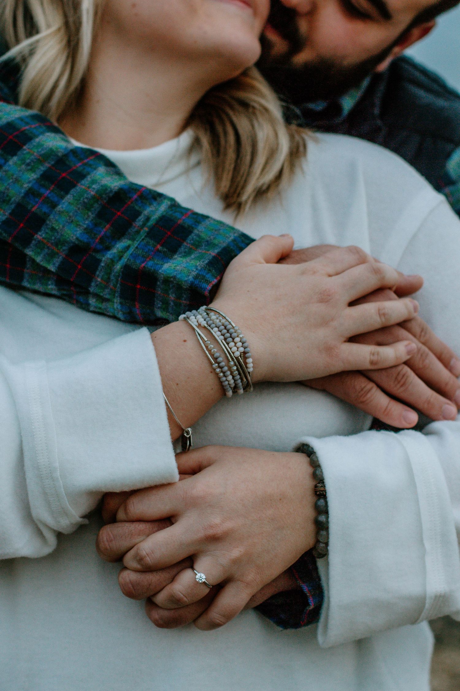 Close-up of engaged couple embracing, showing diamond engagement ring and stacked bracelets.