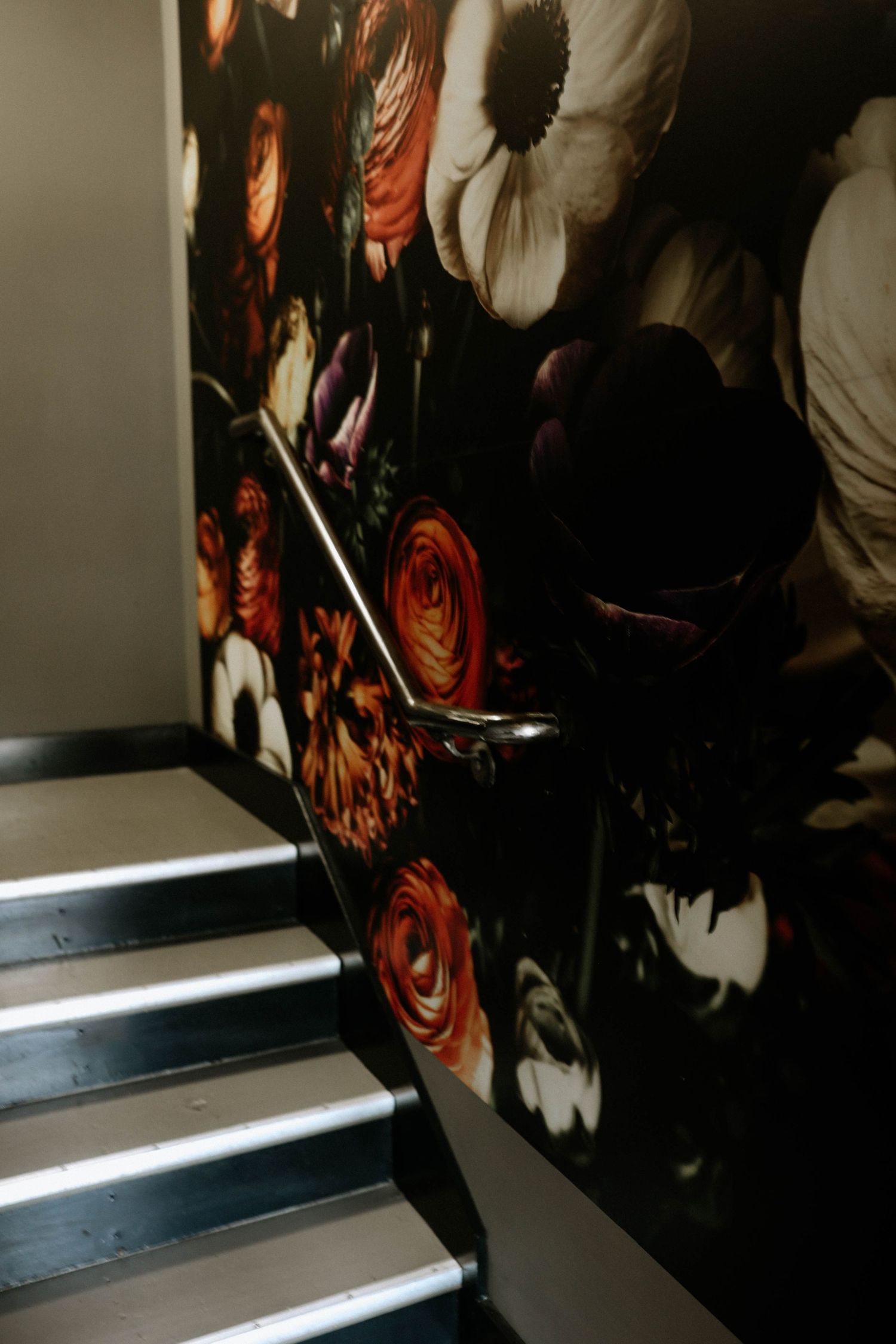 Dramatic staircase with dark floral wallpaper featuring bold orange roses and white blooms, accented by a sleek metal handrail.