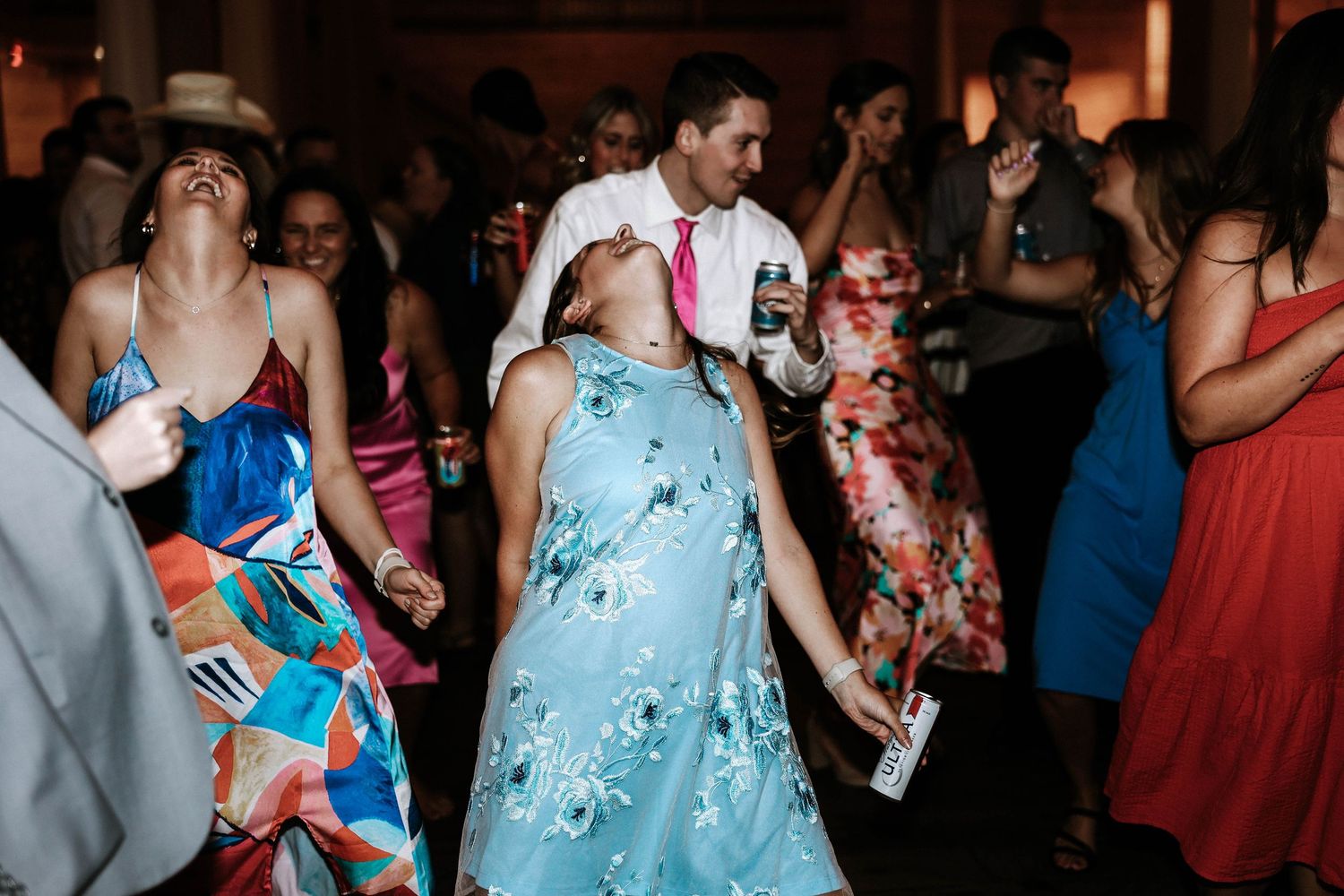 Guests dancing joyfully at a wedding reception, wearing colorful floral dresses and festive attire.