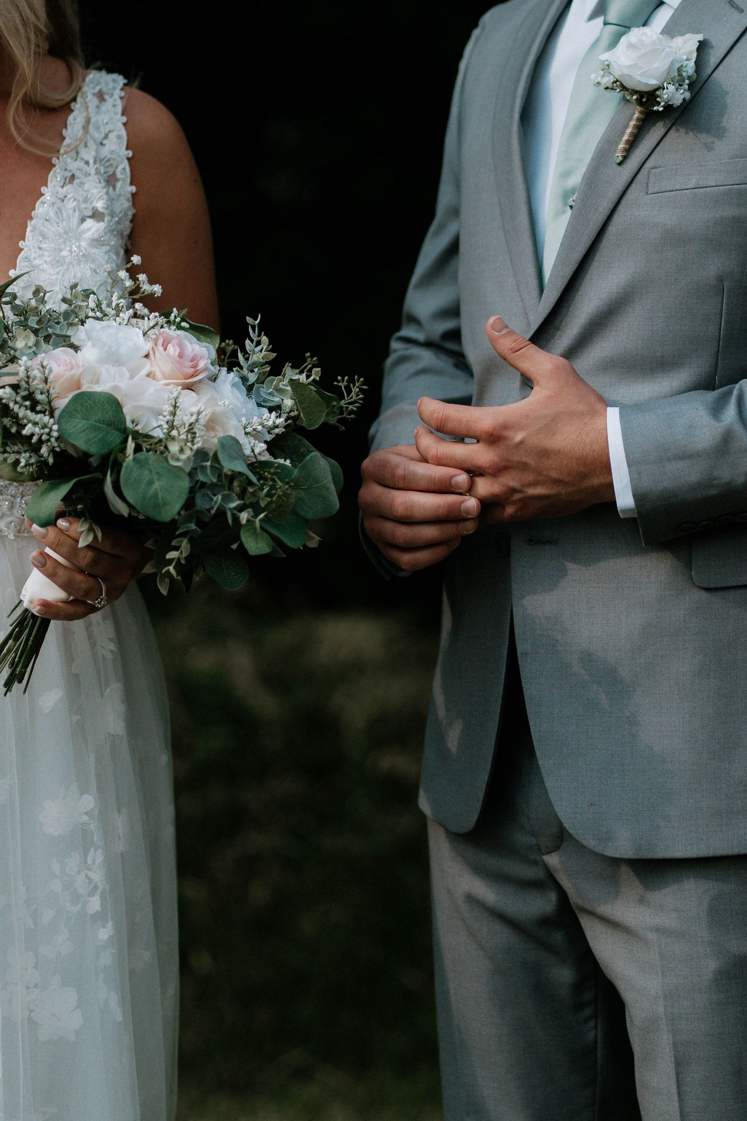 Bride and groom holding hands, bride holding a white and pink floral bouquet, groom in a gray suit with boutonniere.