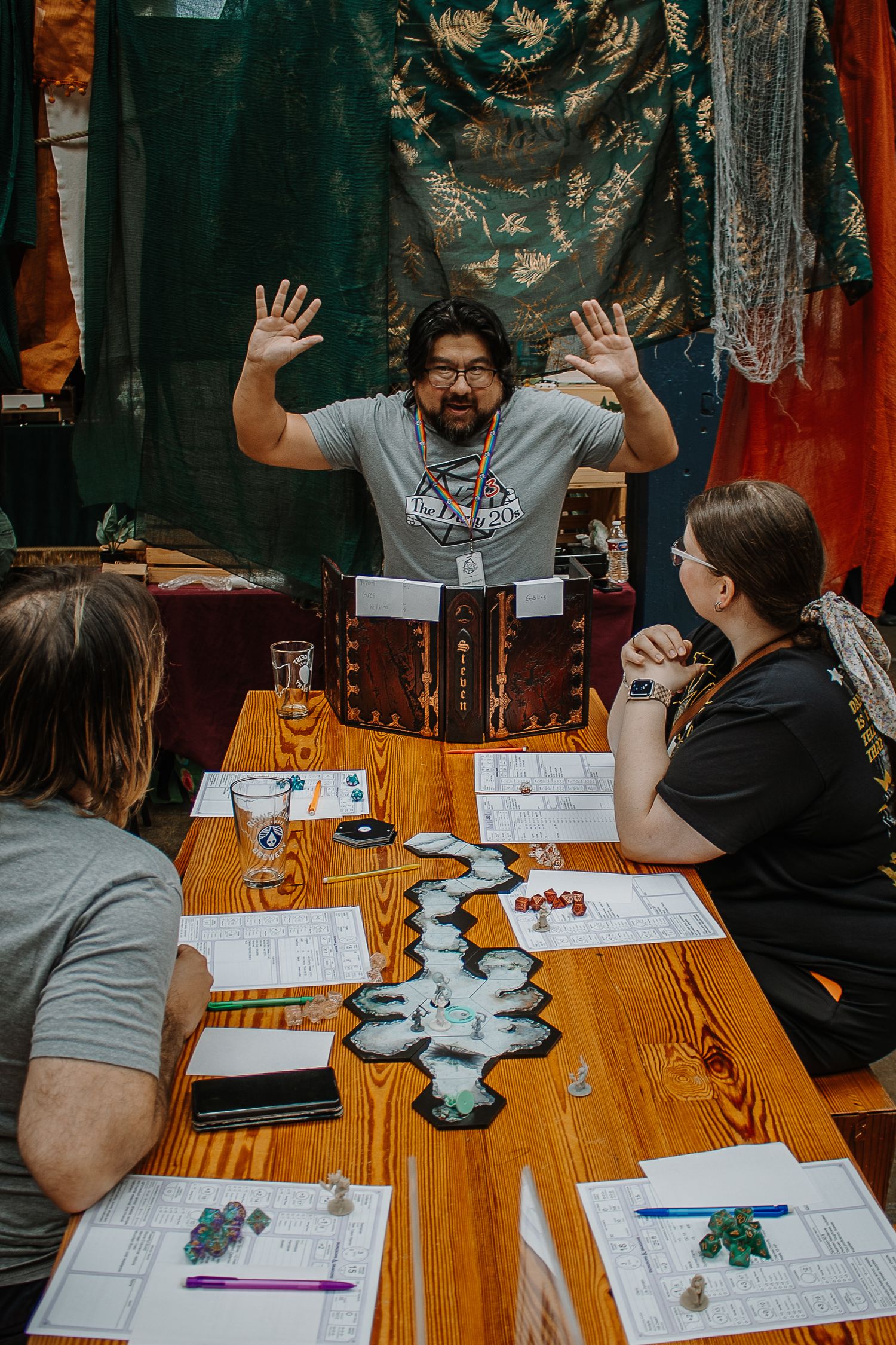 Dungeon master with raised hands leads a tabletop RPG game session with players around a wooden table.