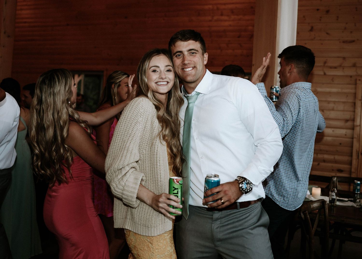 Couple smiling and holding drinks at an indoor wedding reception party.