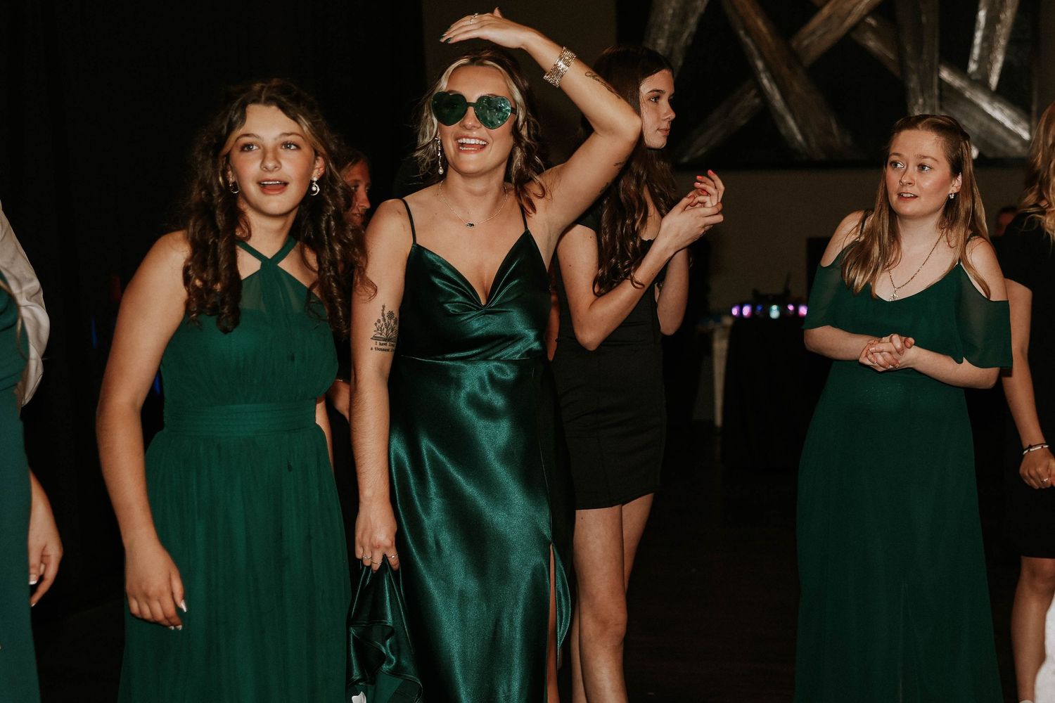 Women in emerald green dresses dancing at a formal event, with one wearing a satin slip dress and sunglasses.