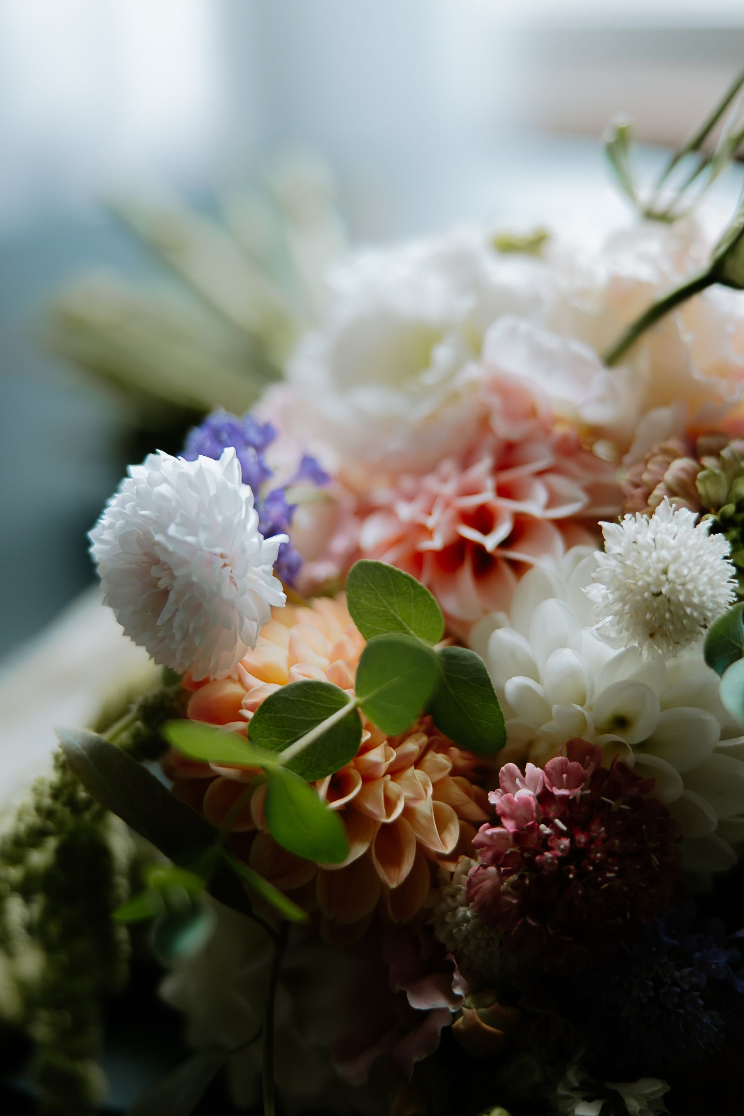Elegant bridal bouquet featuring white, peach, and purple flowers with lush green foliage.