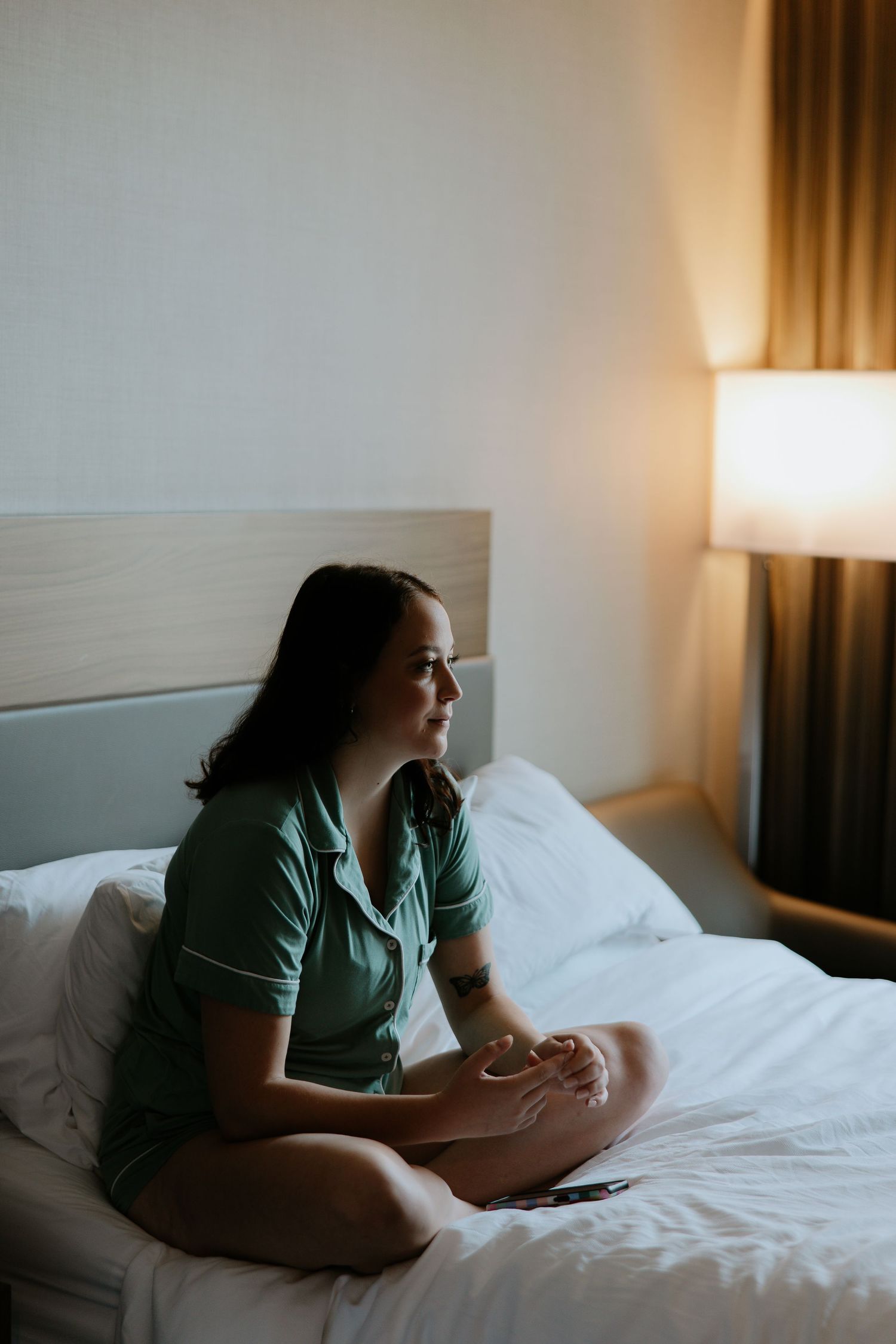 Woman in green pajamas sitting cross-legged on a hotel bed beside a glowing lamp.