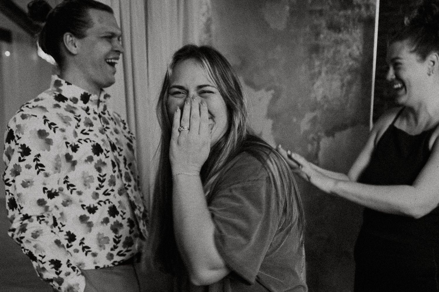 Black and white photo of three people laughing together at an indoor event.
