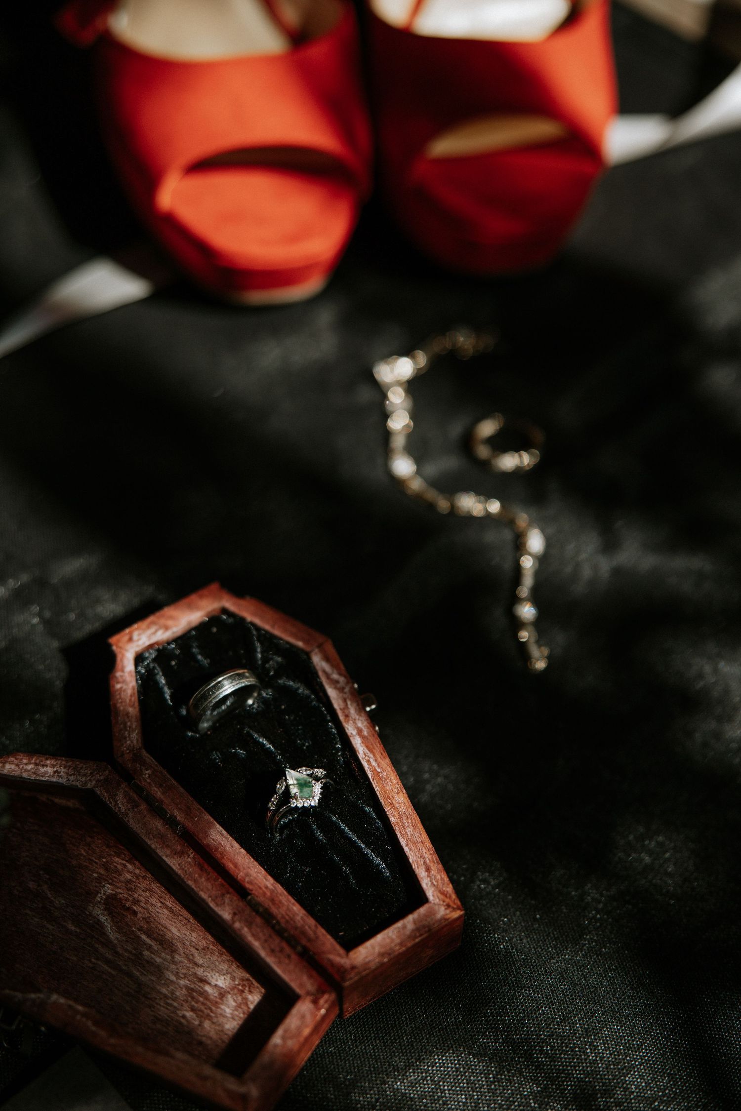 Gothic wedding rings in a coffin-shaped wooden box with red heels and jewelry on dark fabric backdrop.