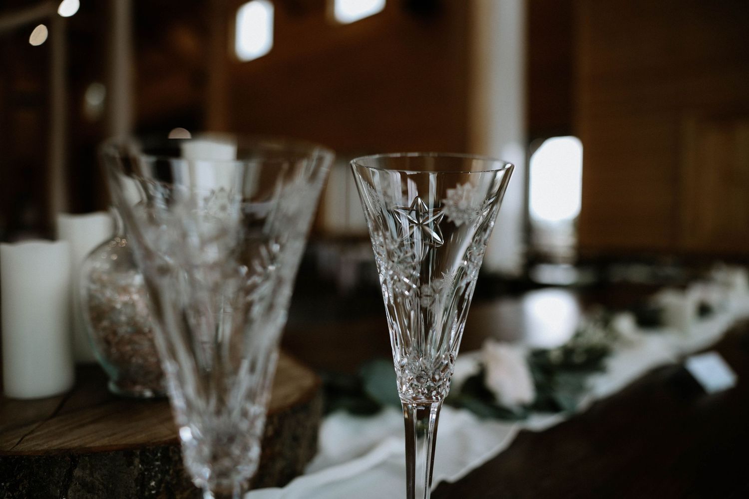 Crystal champagne flutes and glassware on rustic wooden table with white candles at elegant wedding reception.