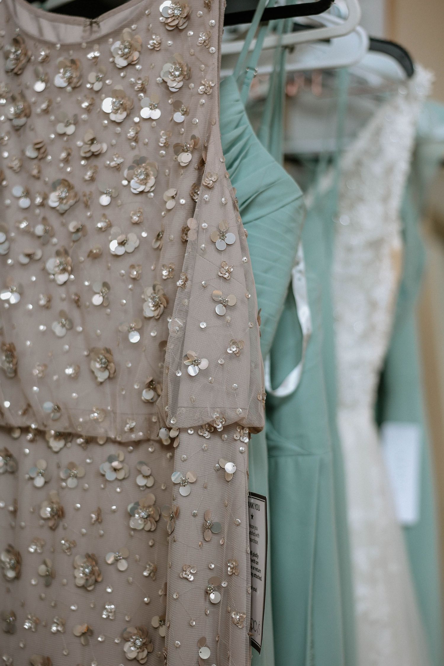 Sequined champagne and mint green bridesmaid dresses hanging on a rack, adorned with floral embellishments.