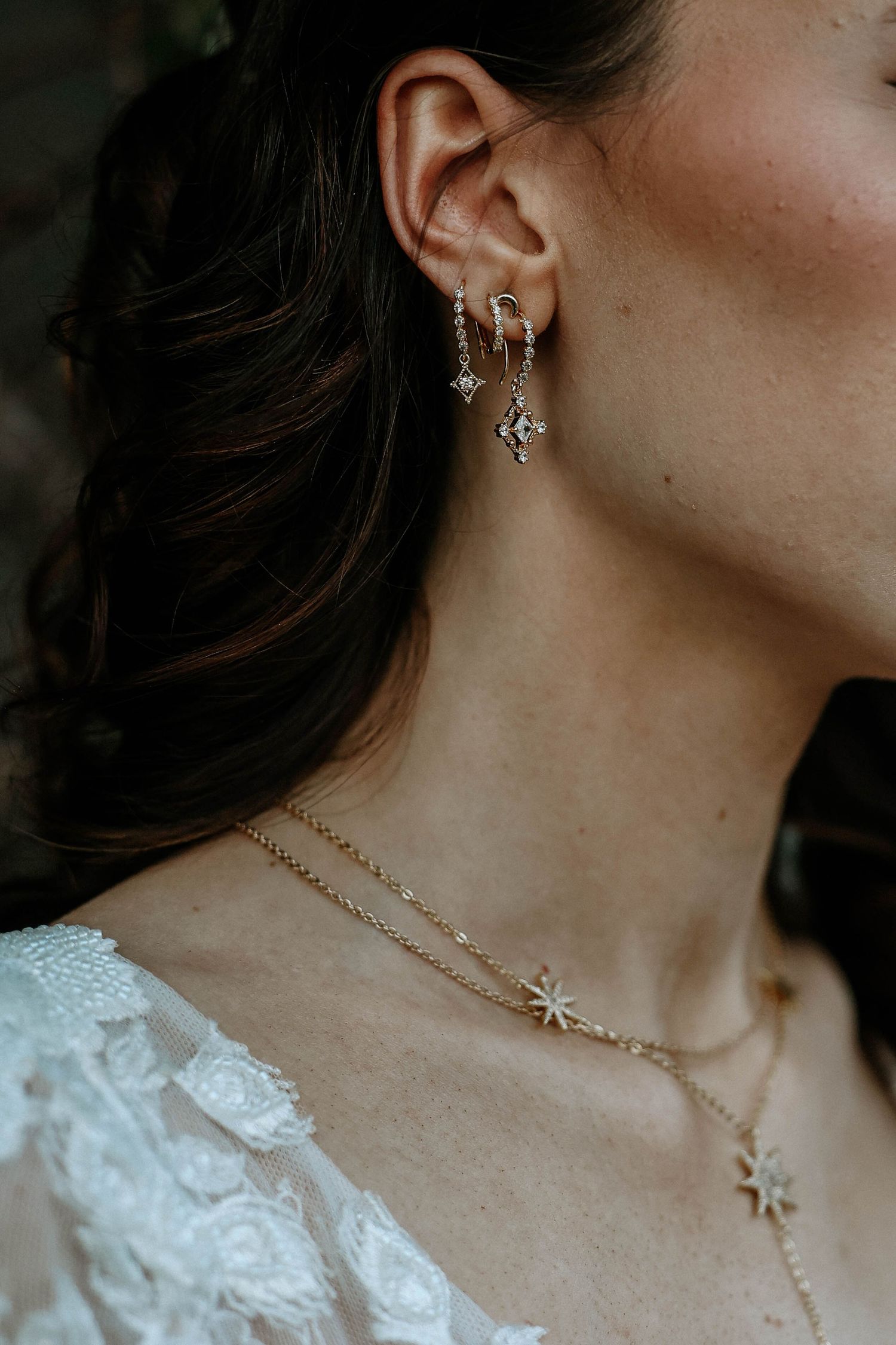 Bride wearing gold star charm earrings with multiple ear piercings and layered gold star pendant necklaces.