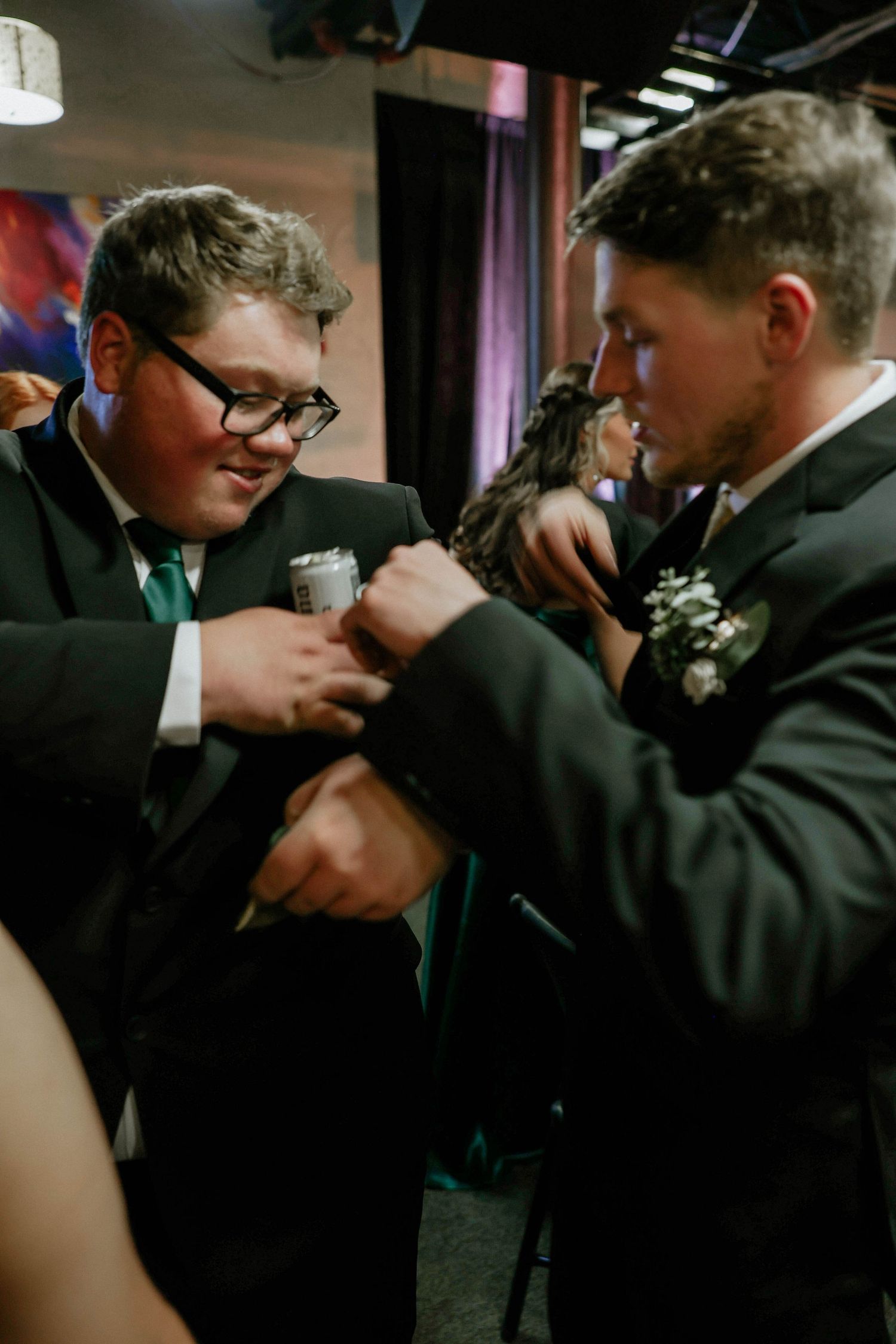Two young men in black suits adjusting cufflinks at a formal wedding event.