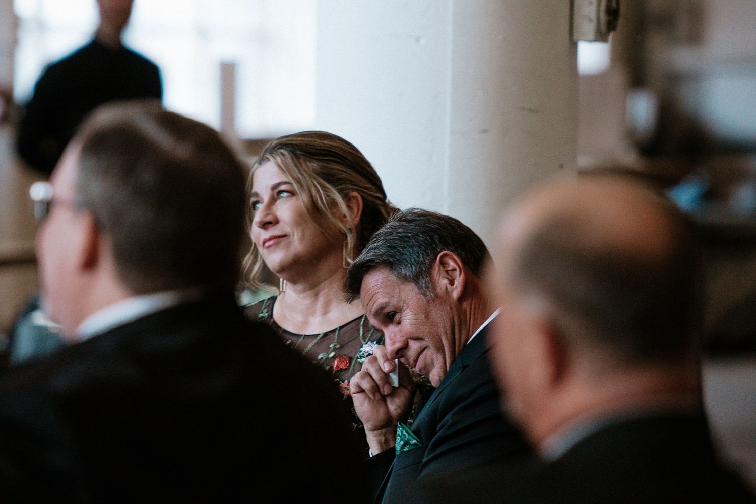 Emotional wedding guests watching ceremony, man wiping tears while woman looks on tenderly at The Red Space in Cleveland, Ohio