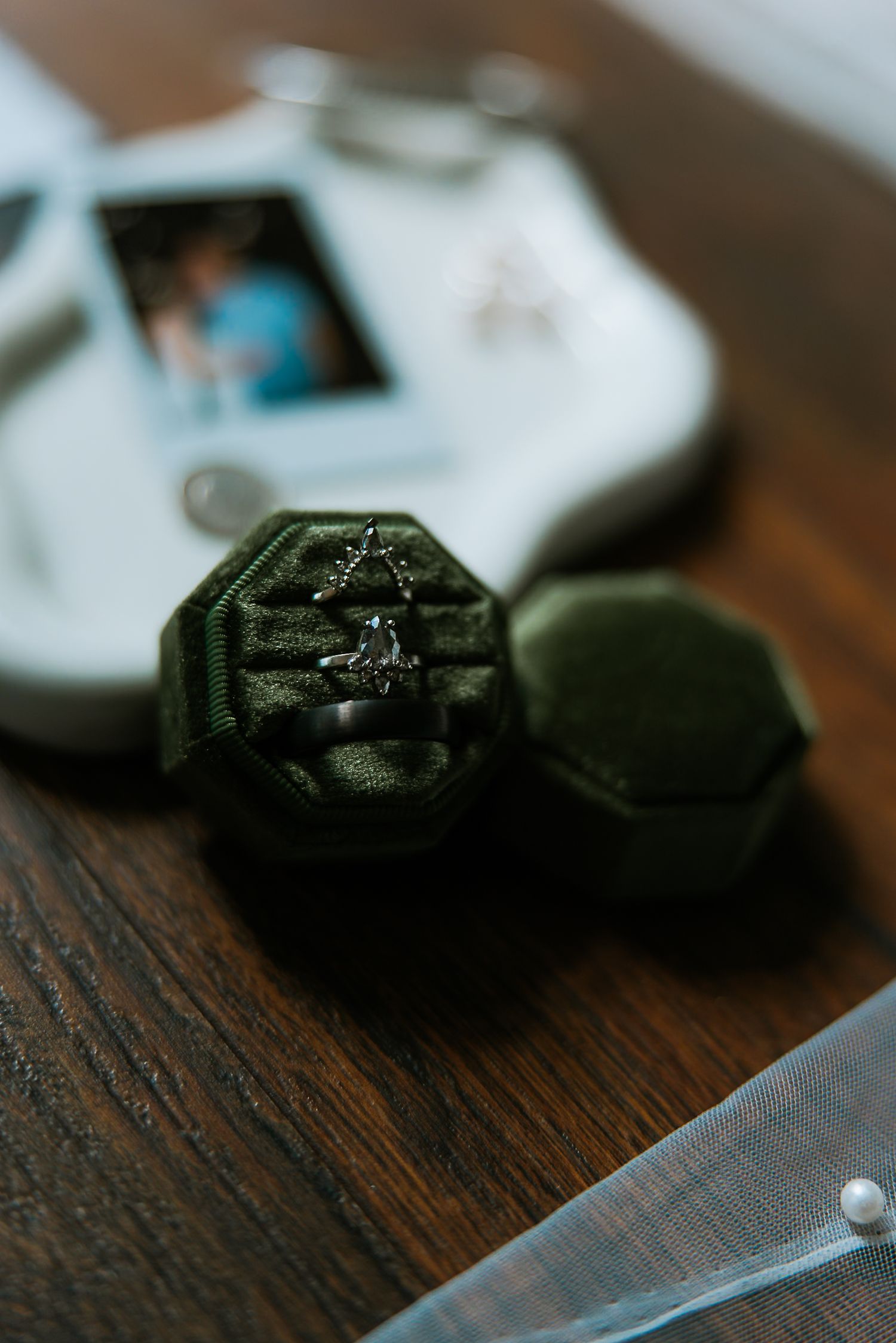 Wedding rings nestled in an open green velvet octagonal ring box on a wooden surface.