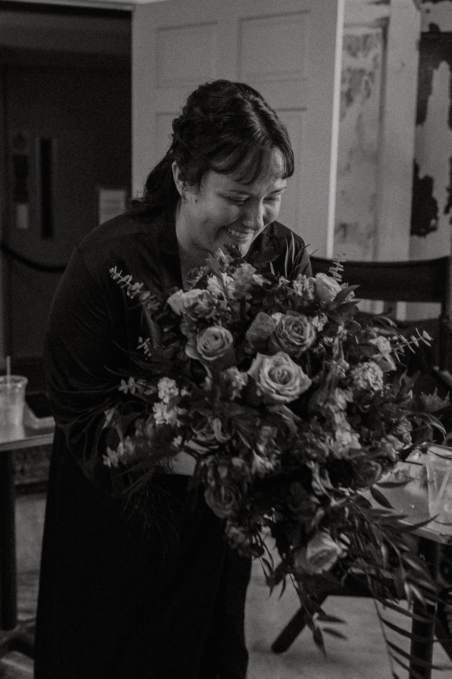 Bride smiles while holding a large lush floral bouquet in black and white photo.