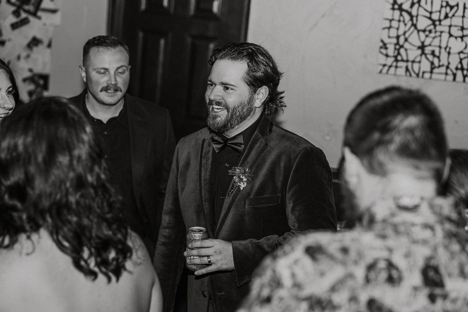 Bearded man in dark suit smiling at wedding guests in black and white photo.